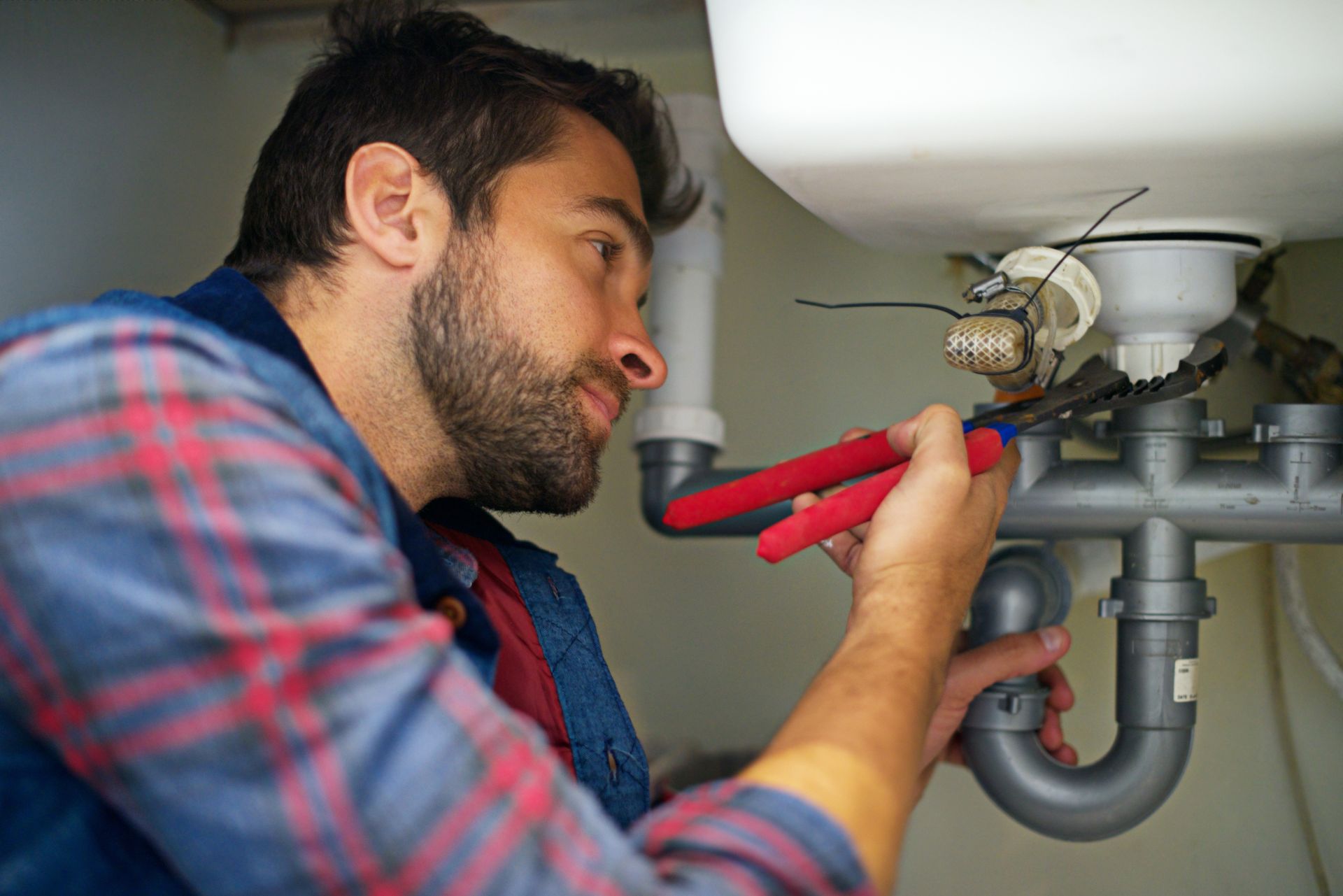 Back of a plumbing repair contractor holding a red toolbox to perform a repair job in the kitchen.