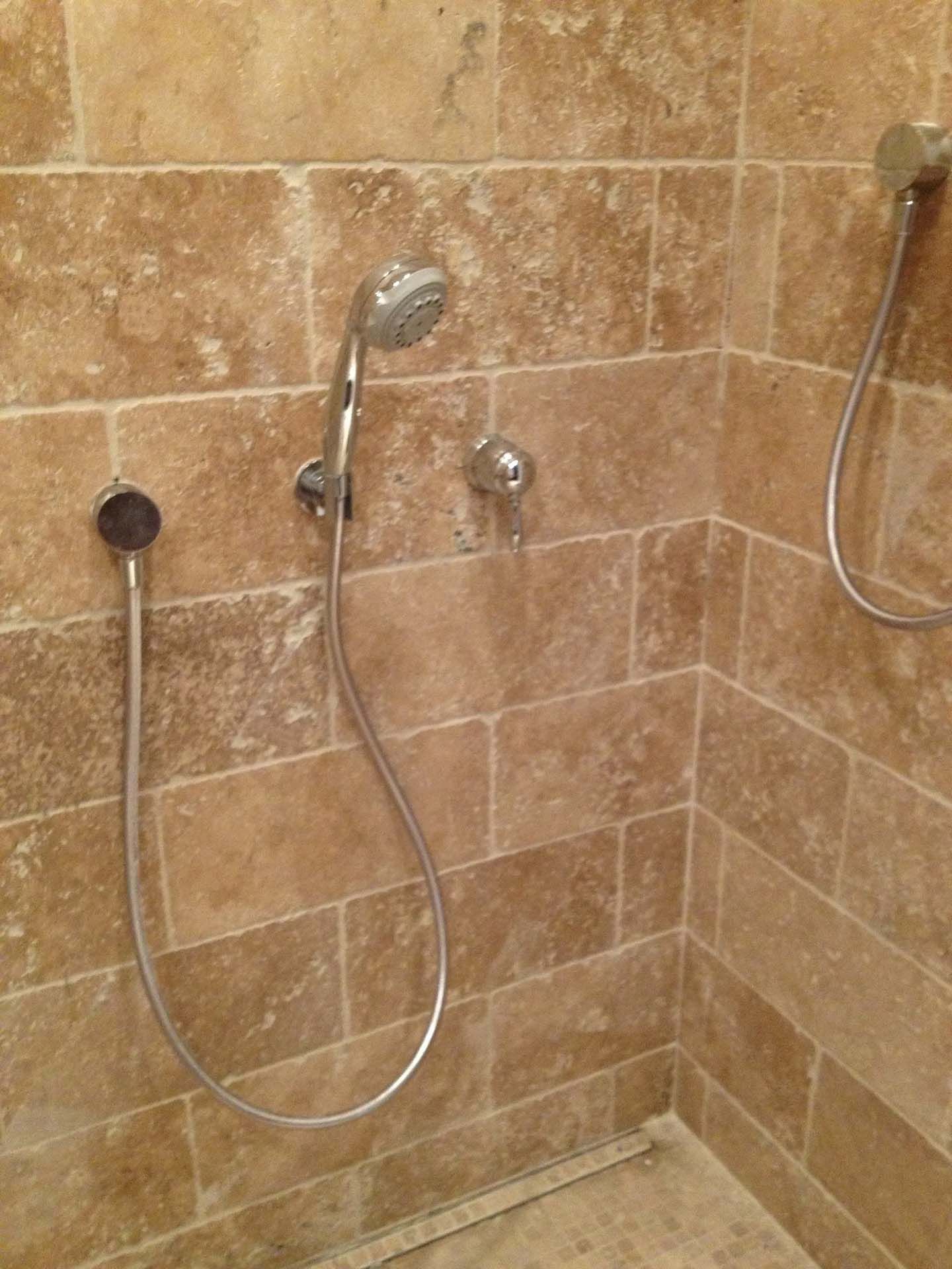 Shower stall with beige stone tile and two handheld showerheads
