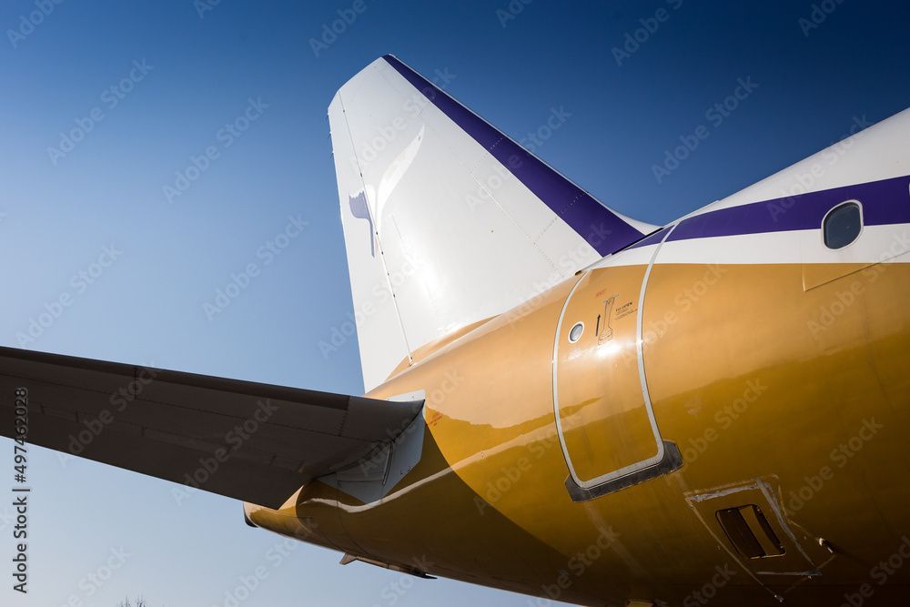 The tail of a yellow and purple airplane with a blue sky in the background.