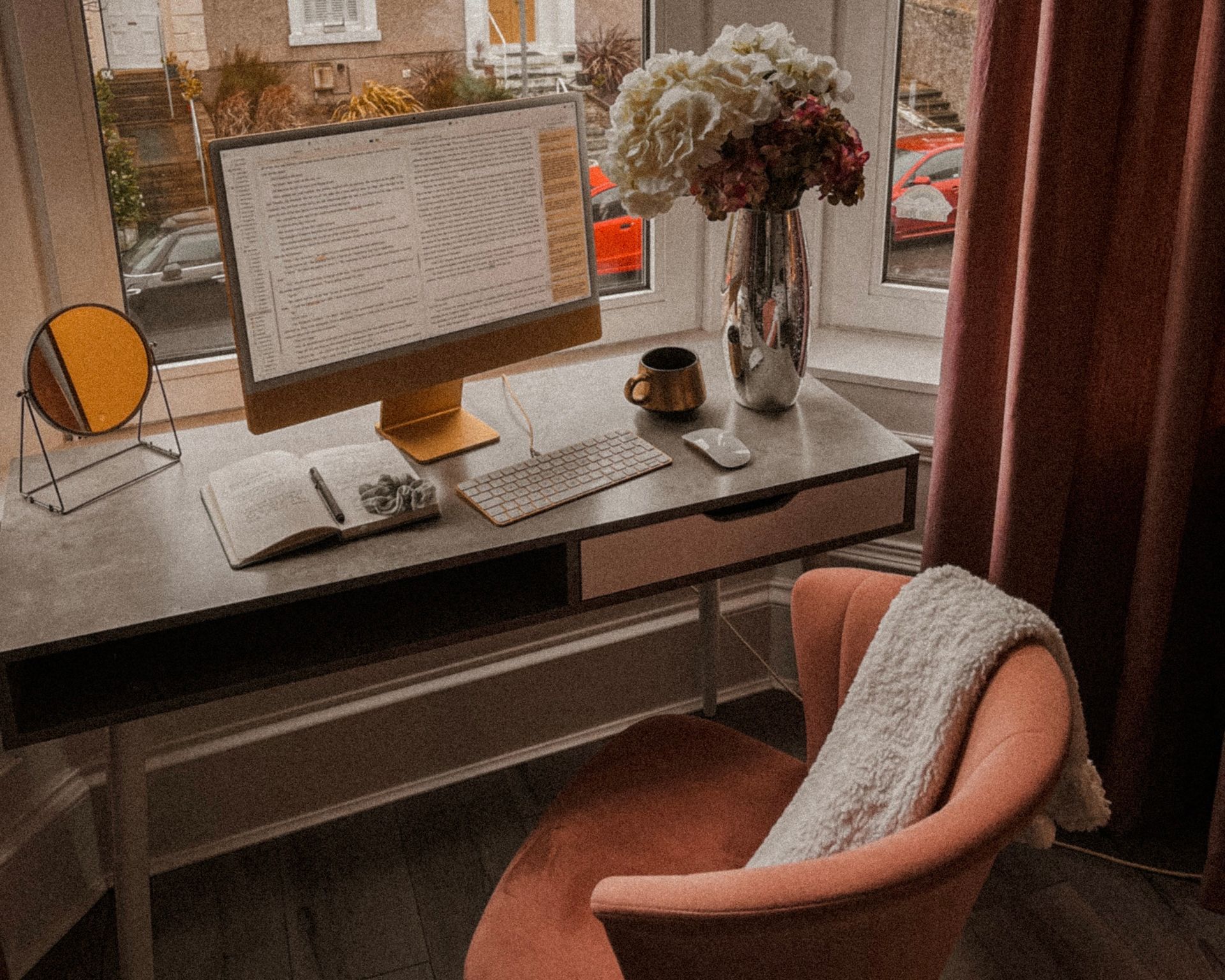 Pink chair at a cosy desk. On the desk is a yellow iMac with words on the screen.