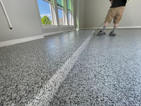 A man is cleaning a garage floor with a mop.