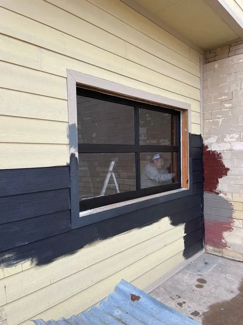 A man is painting a window on the side of a building.