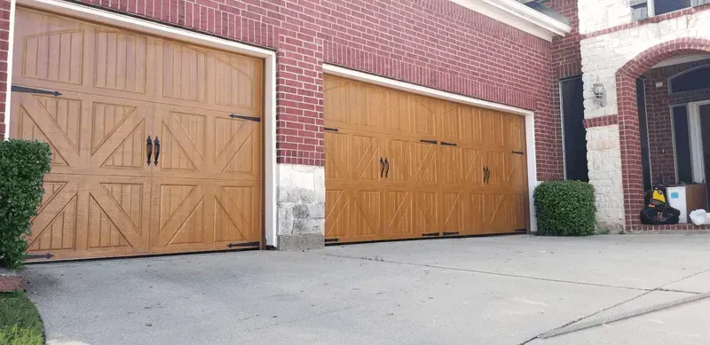 Two wooden garage doors are sitting in front of a brick building.