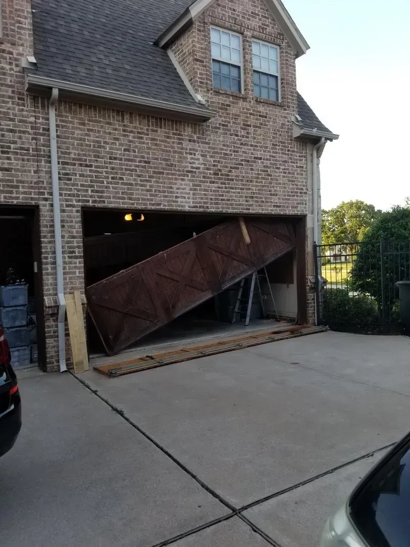 A car is parked in front of a brick house with a broken garage door.