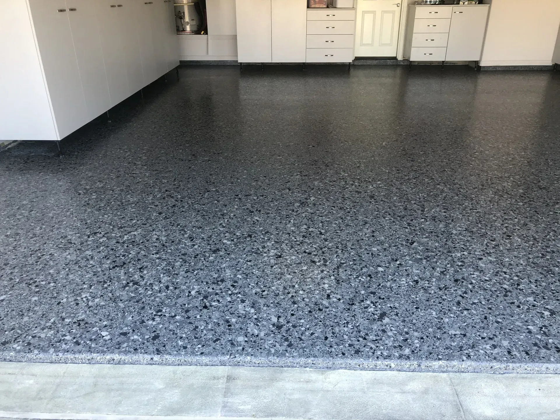 A garage with a gray concrete floor and white cabinets.