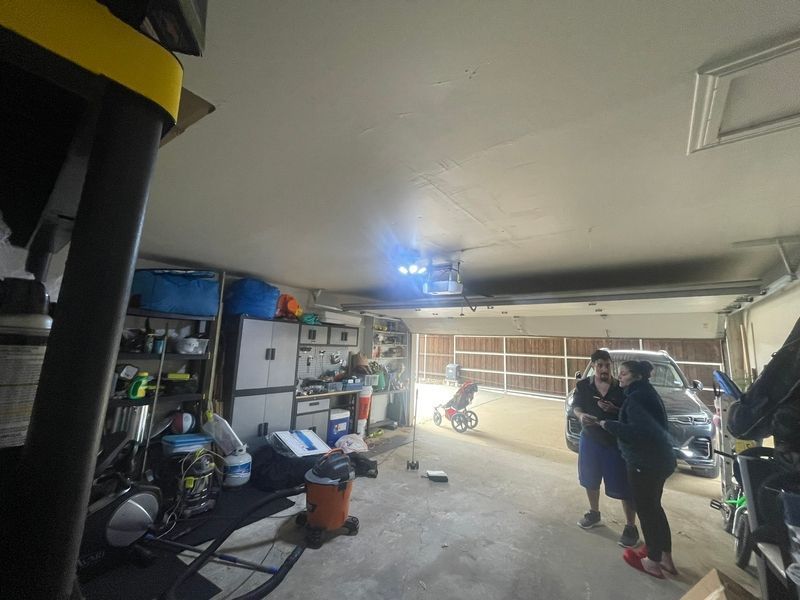 A group of people are standing in a garage with a projector hanging from the ceiling.
