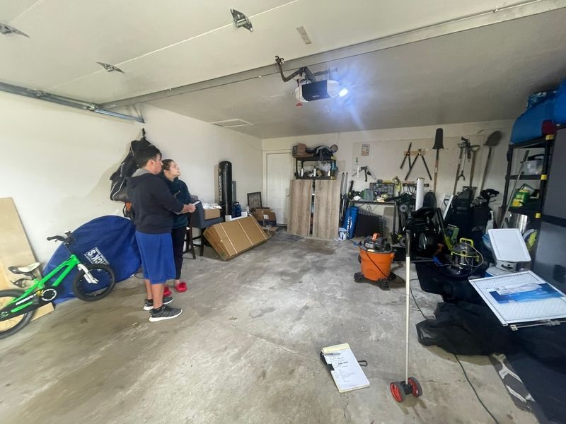 A man is standing in a garage with a bicycle and a vacuum cleaner.