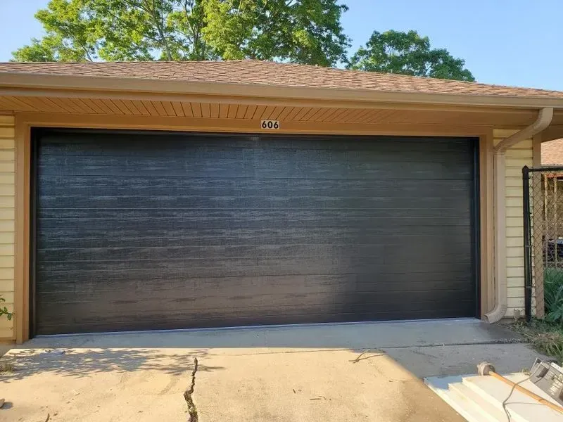 A black garage door is sitting in front of a house.