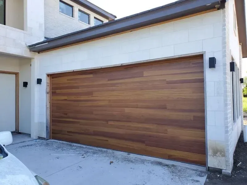 A wooden garage door is sitting in front of a white house.