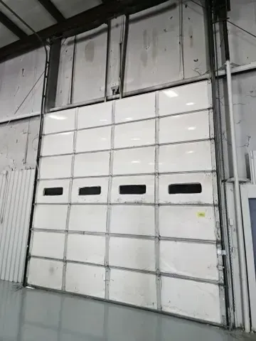 A large white garage door is open in a warehouse.