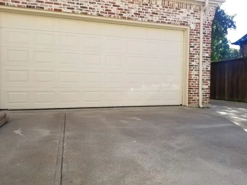 A white garage door is open in front of a brick house.