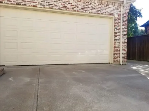 A white garage door is open in front of a brick house.