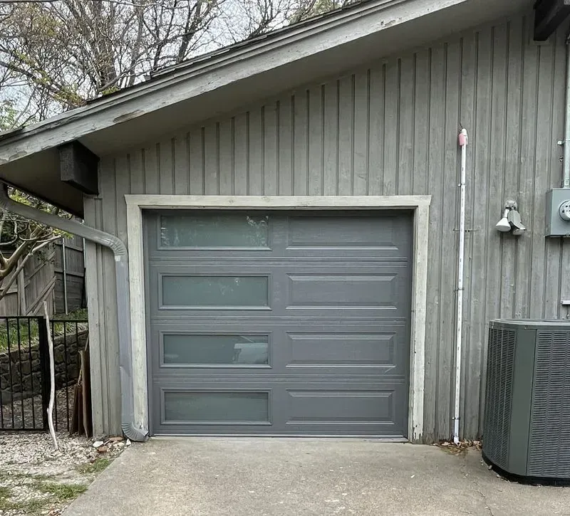 A gray garage door with a gray air conditioner next to it
