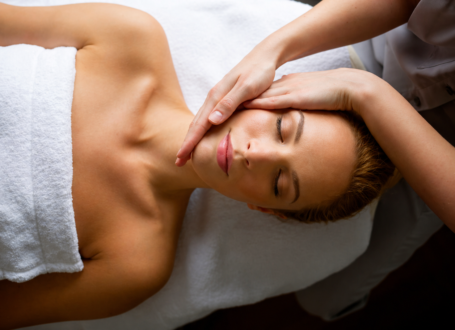 Person receiving a facial massage on a spa table with a white towel and closed eyes