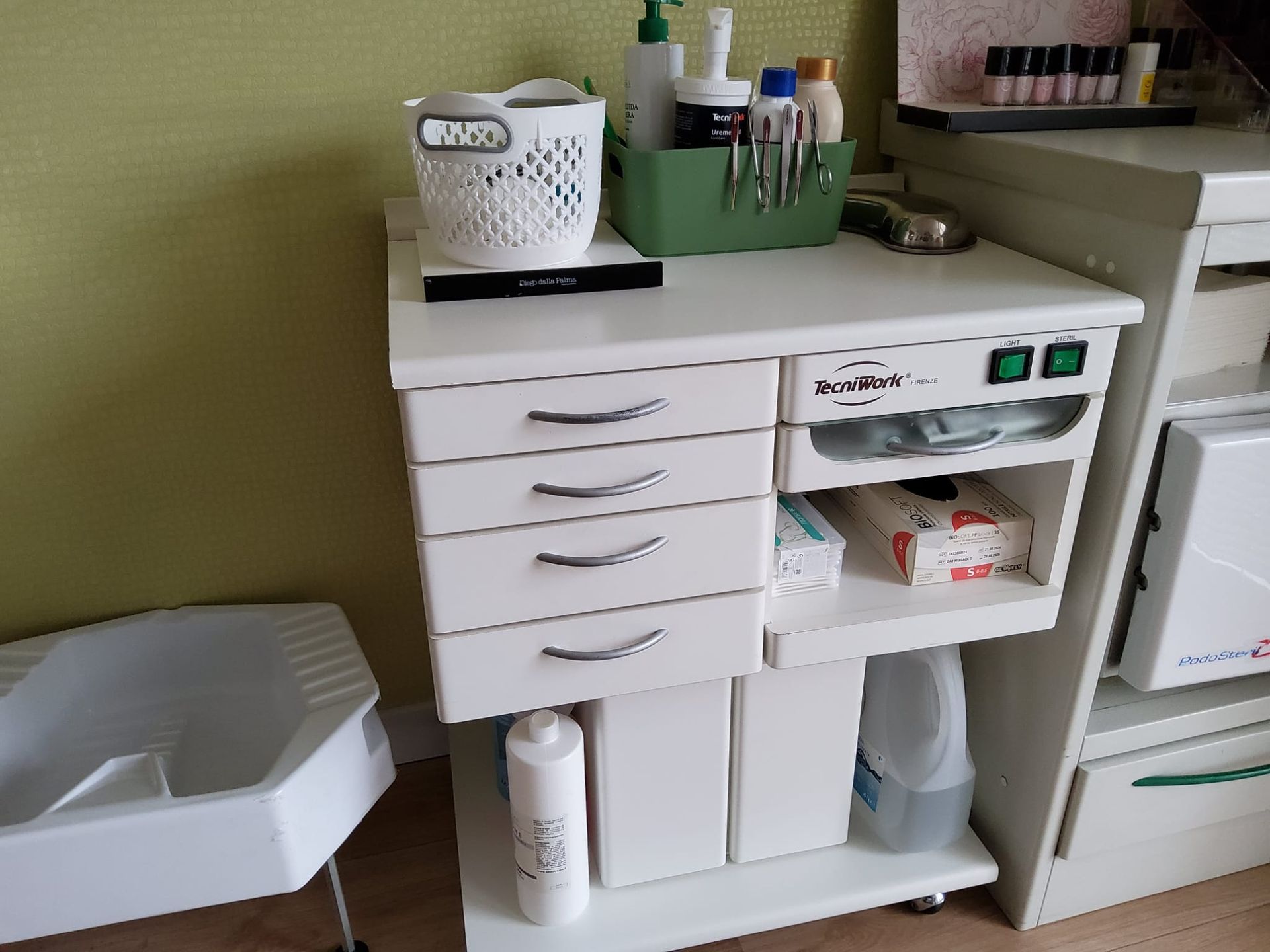 White medical cabinet with drawers, bottles, and supplies in a clinic or salon room