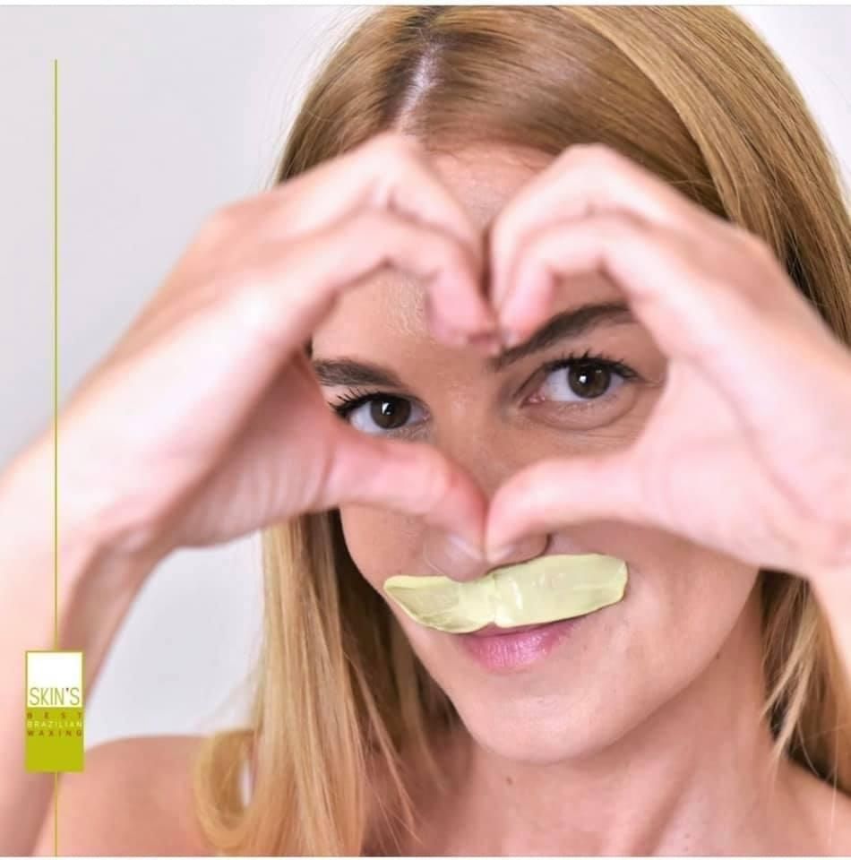 Woman making a heart shape with her hands around her face, with a strip on her upper lip.