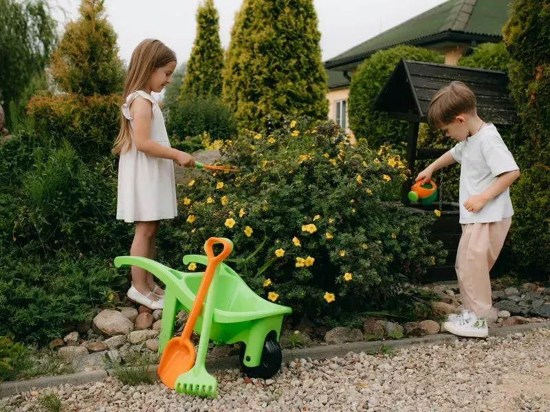 A boy and a girl are playing in a garden with toys.