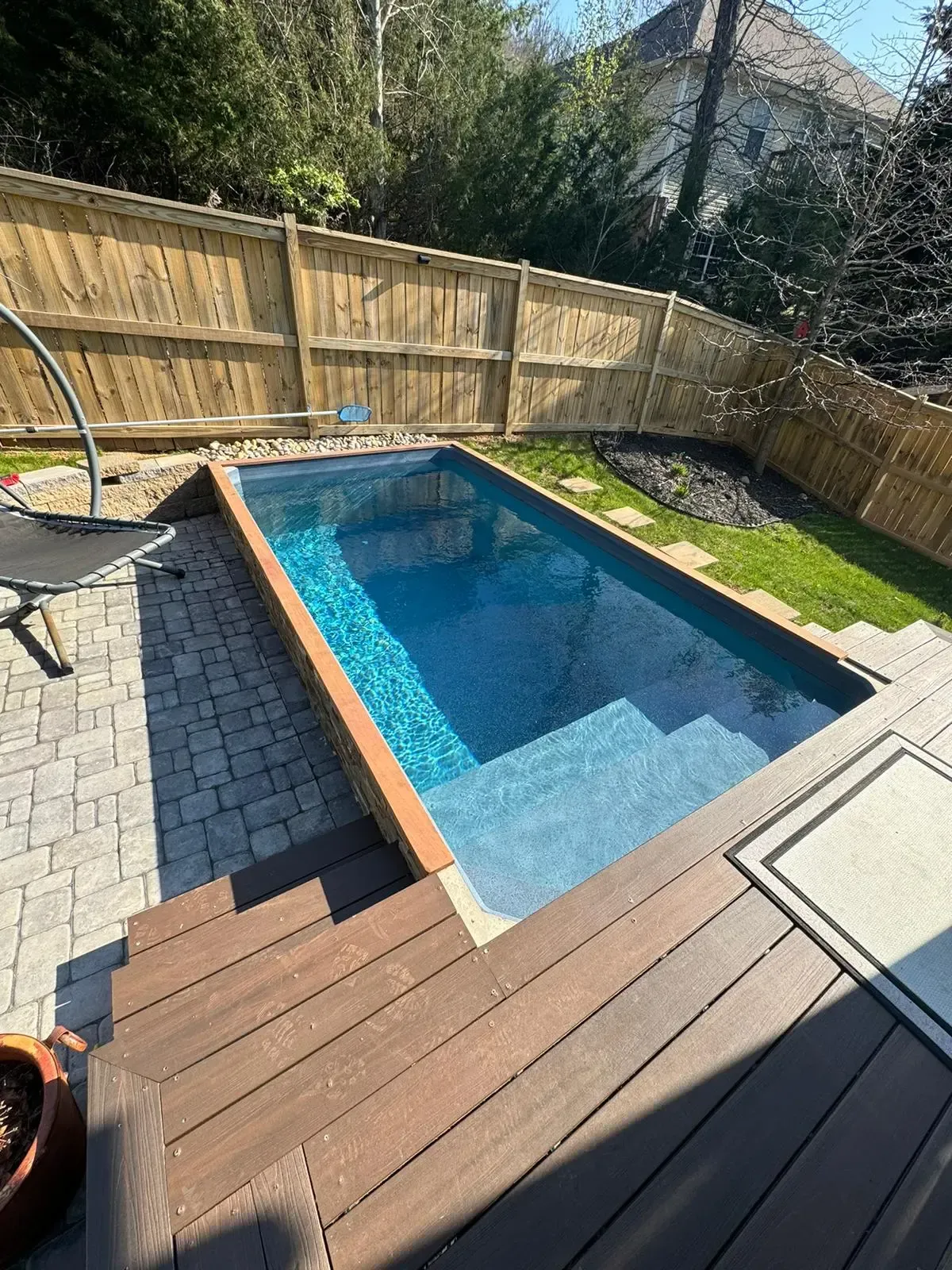 A large swimming pool is surrounded by a wooden fence and a wooden deck.