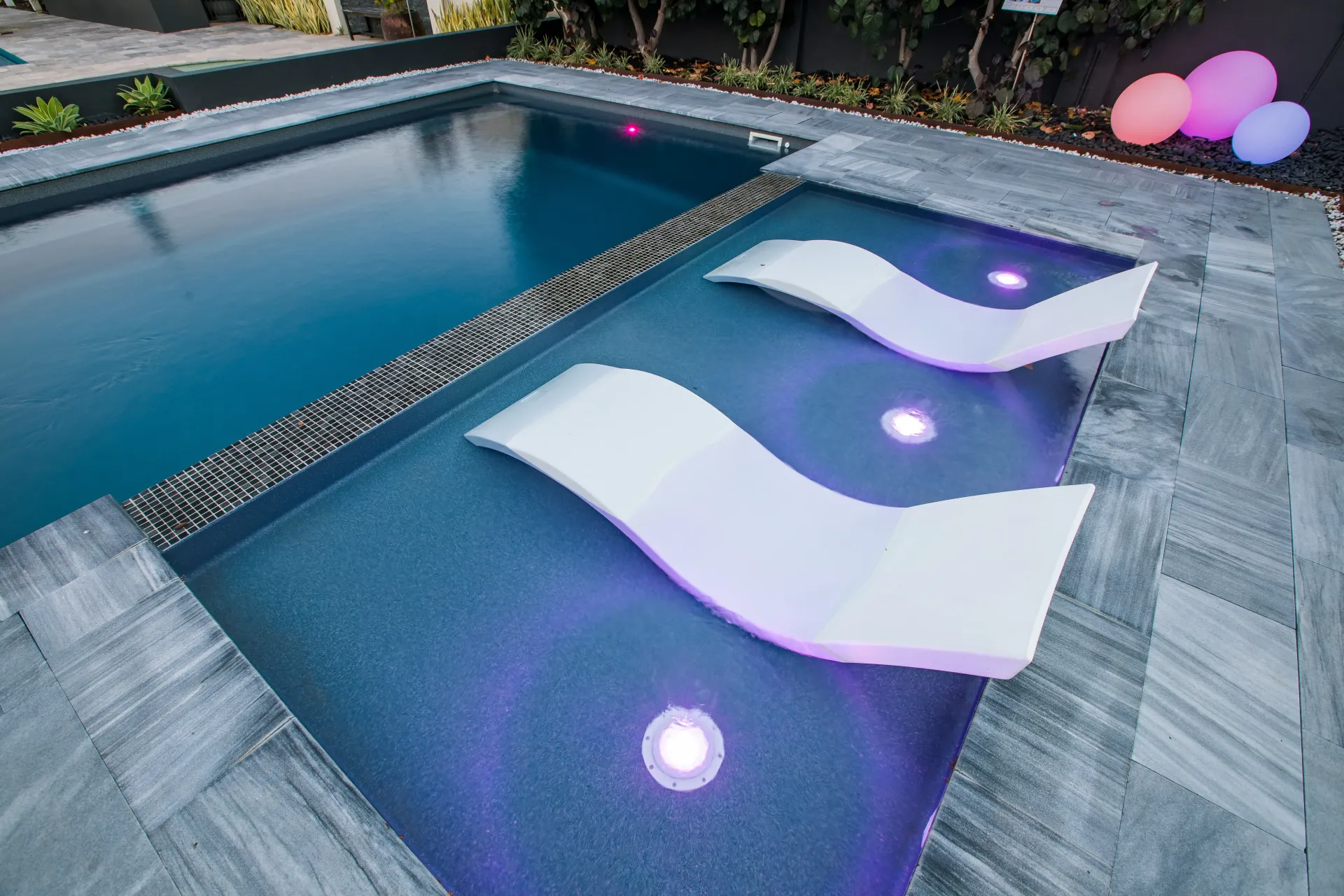 Two lounge chairs are sitting next to a swimming pool with purple lights.