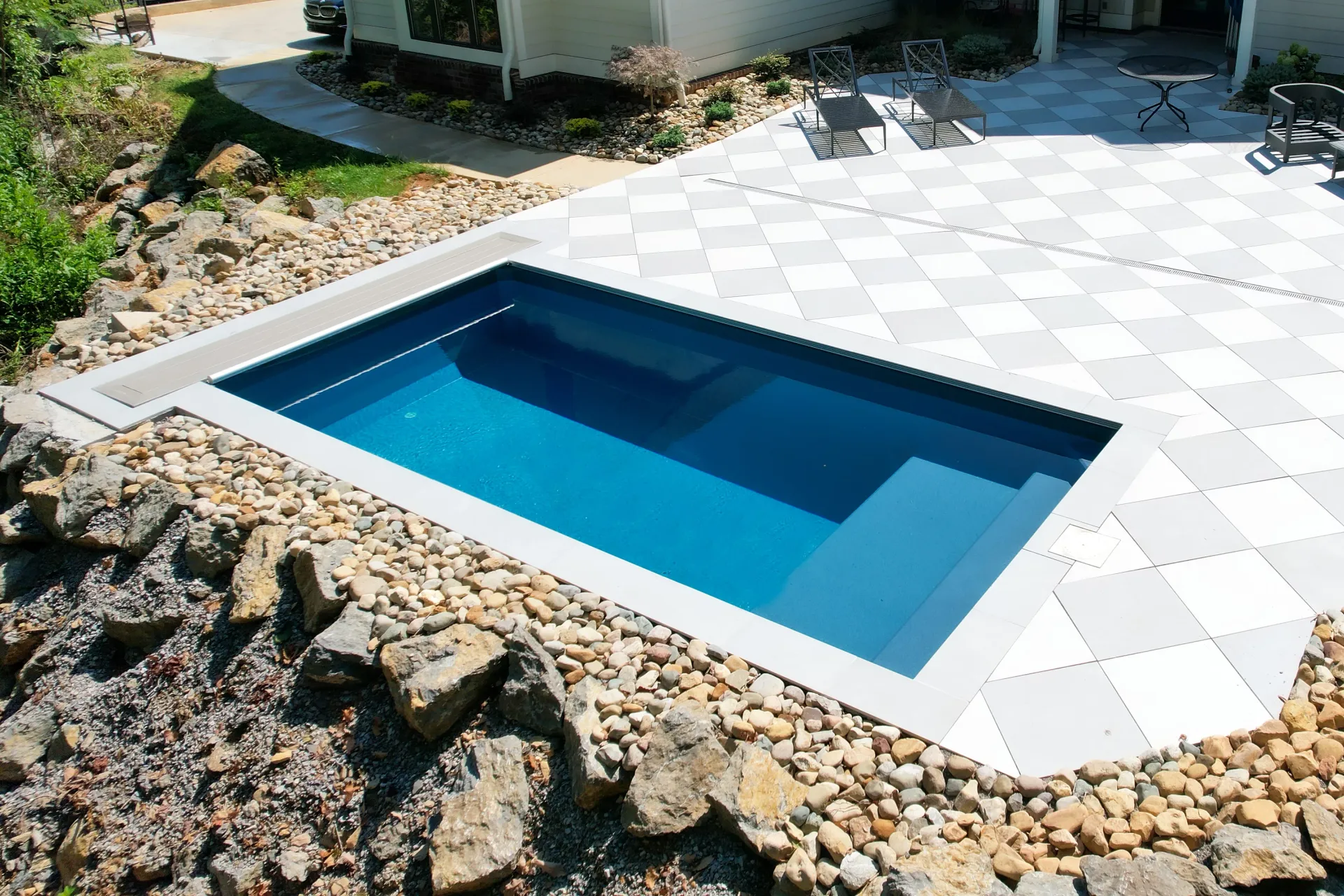 A small swimming pool is surrounded by rocks in front of a house.