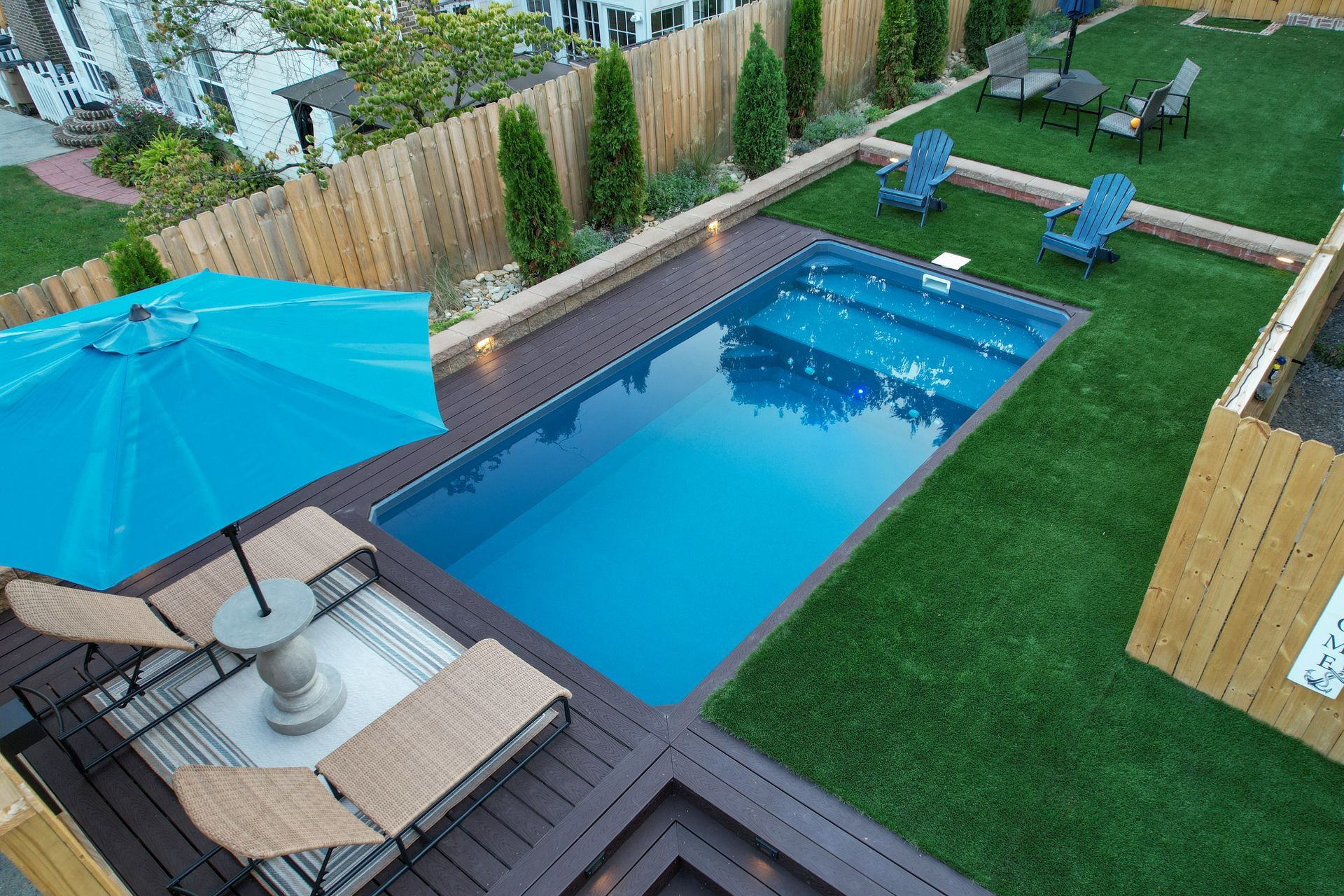 An aerial view of a backyard with a large swimming pool surrounded by chairs and umbrellas.