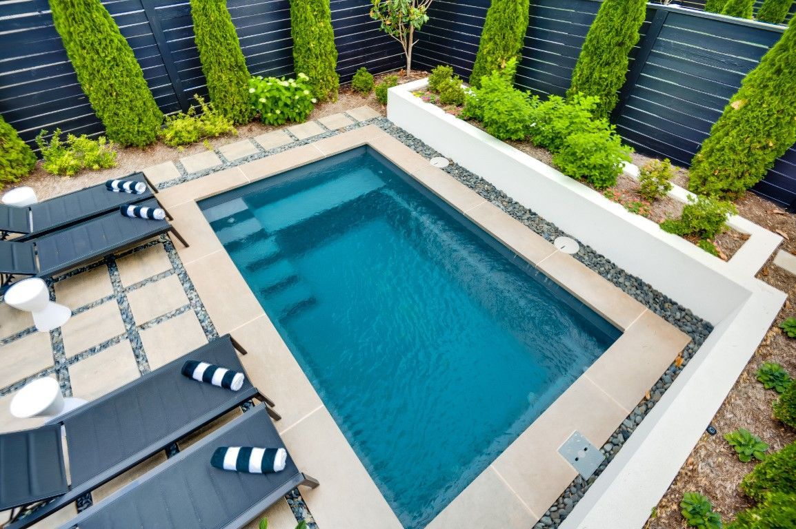 A small swimming pool is surrounded by chairs and a fence.