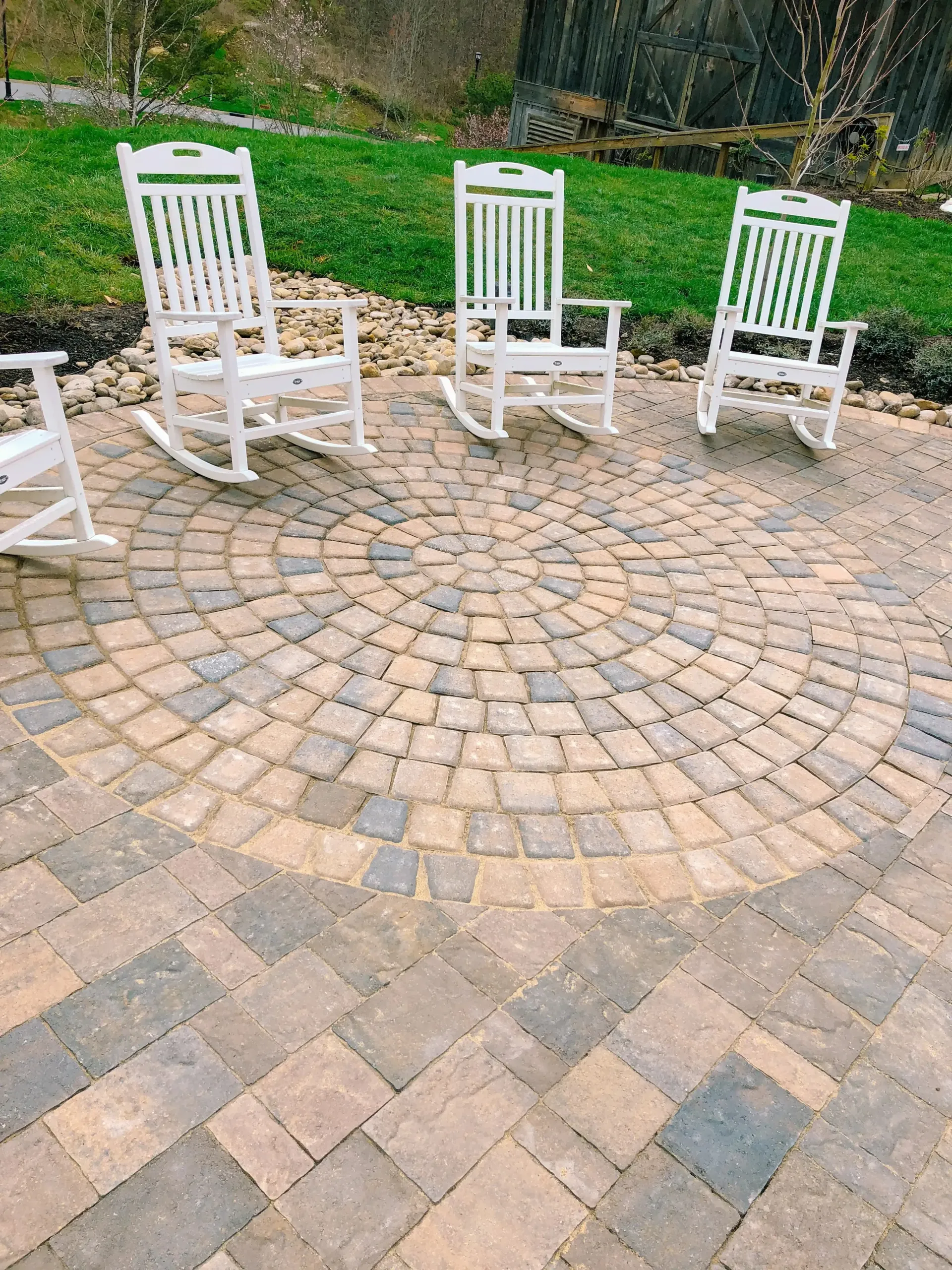 Three white rocking chairs are sitting in a circle on a patio.
