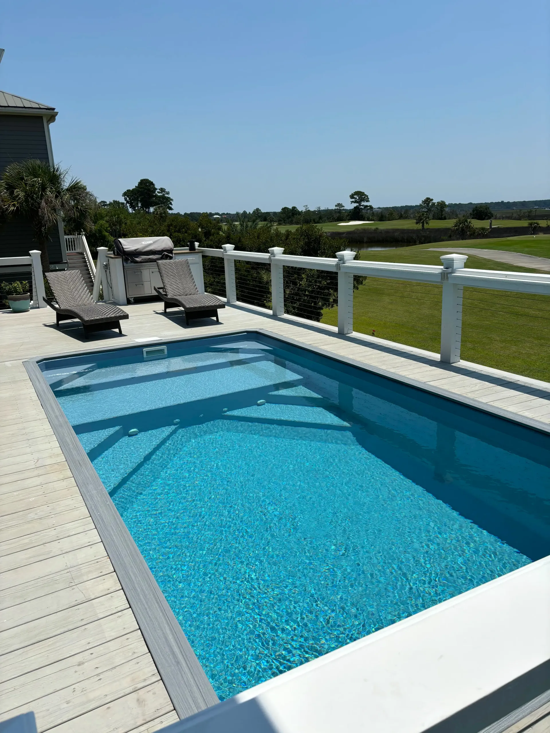 A large swimming pool is surrounded by chairs on a deck