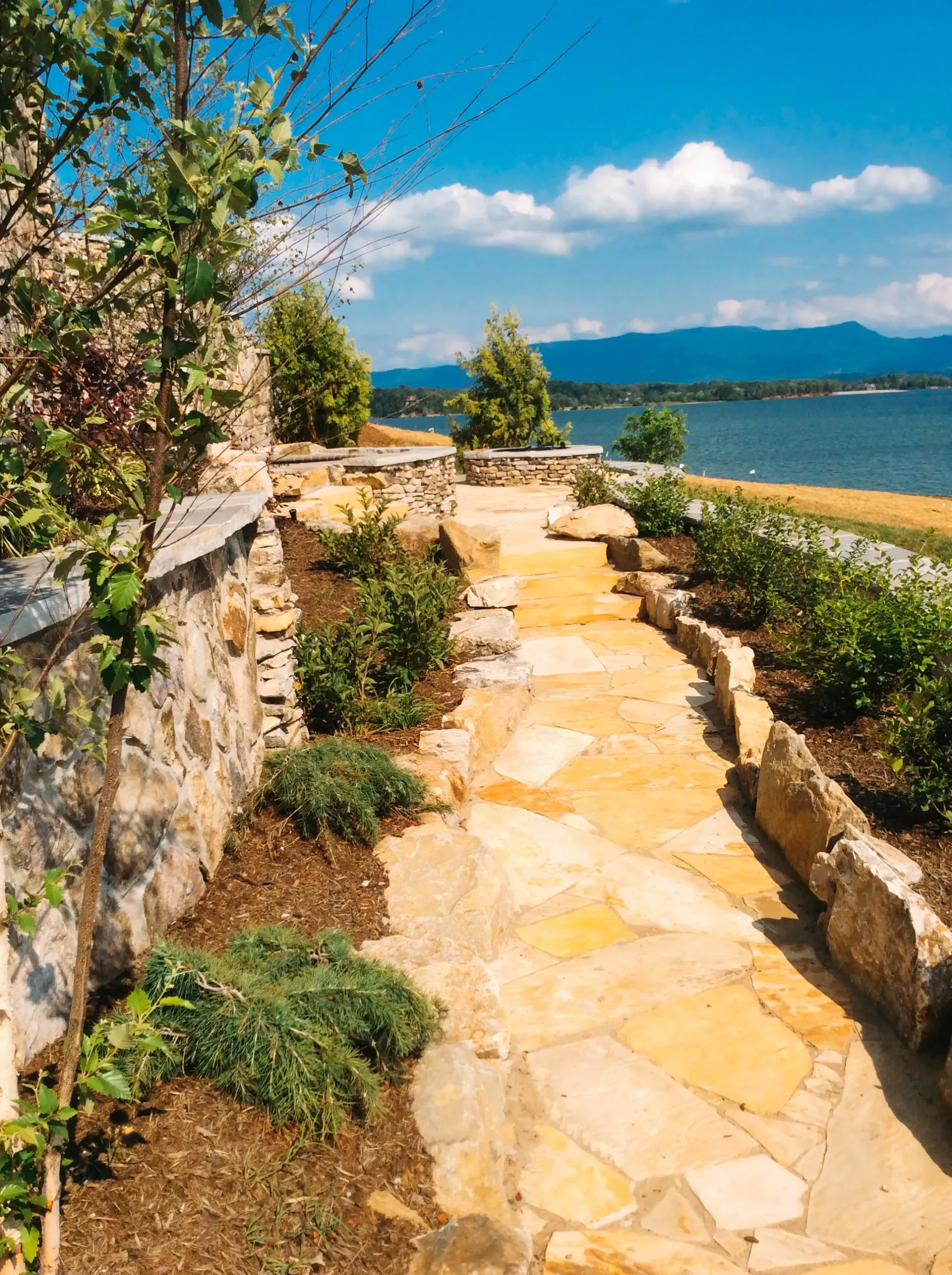 A stone walkway leading to a body of water with mountains in the background