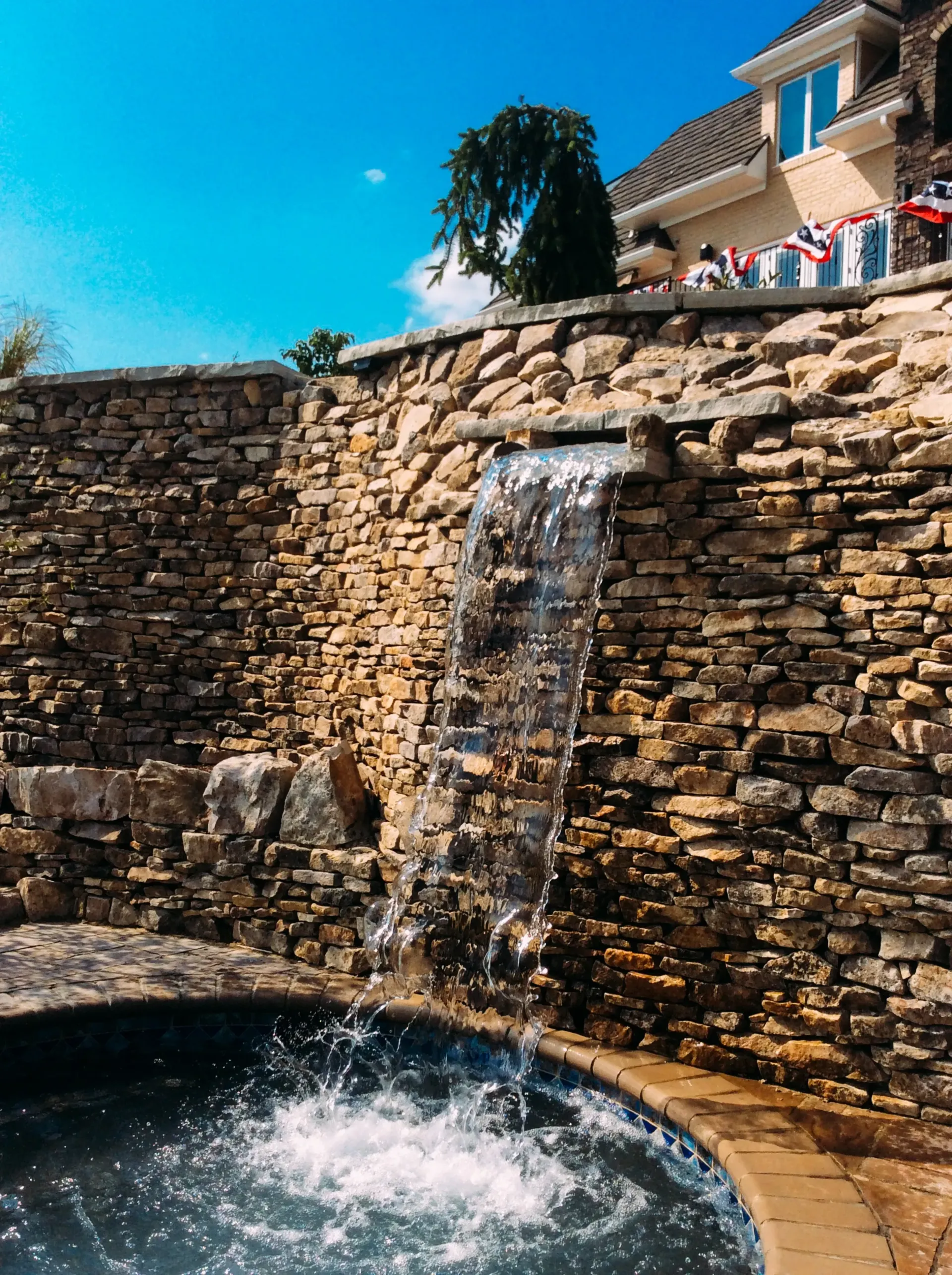 A waterfall is coming down a stone wall next to a pool.