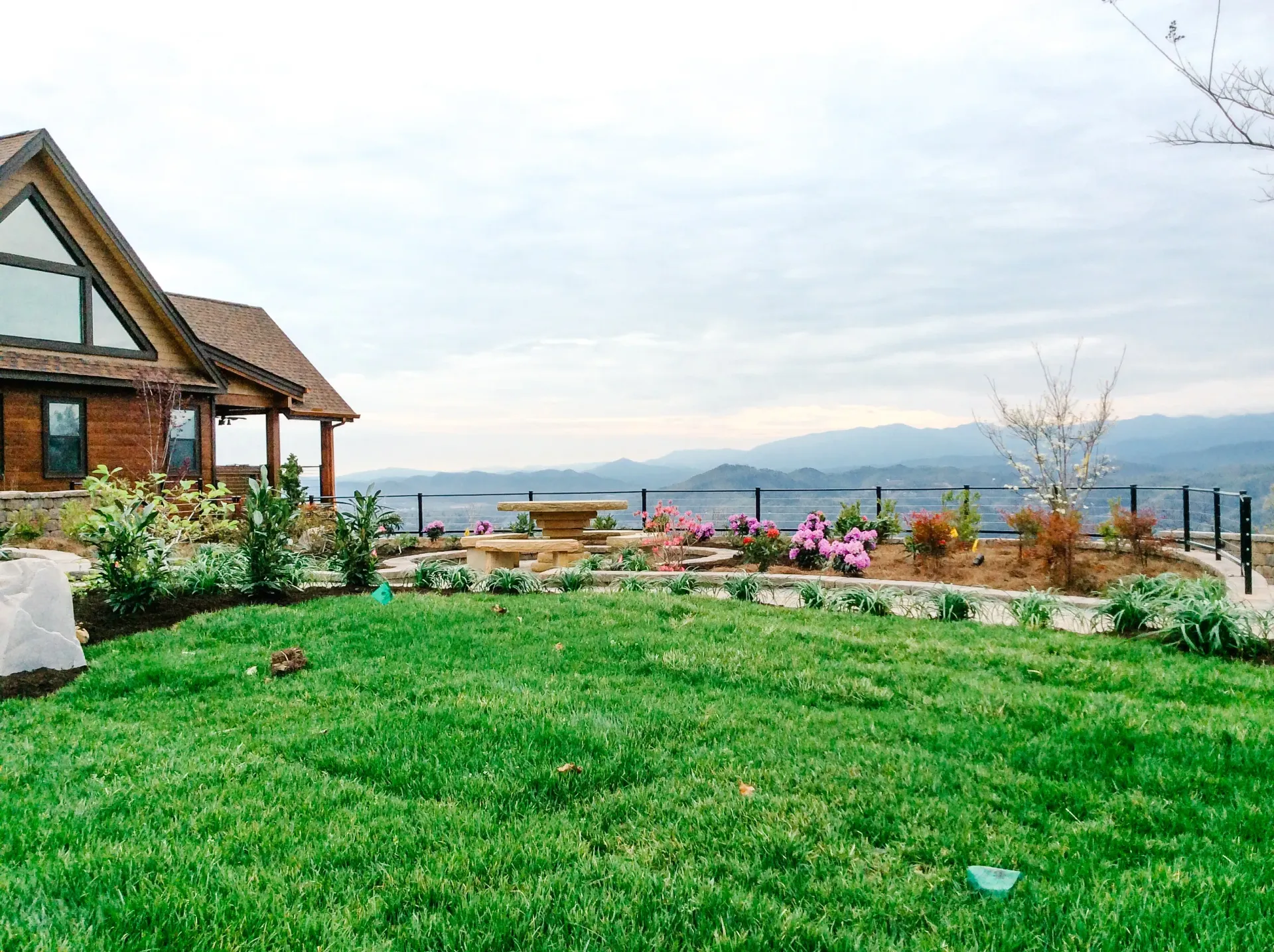 A large lush green lawn in front of a house with mountains in the background.