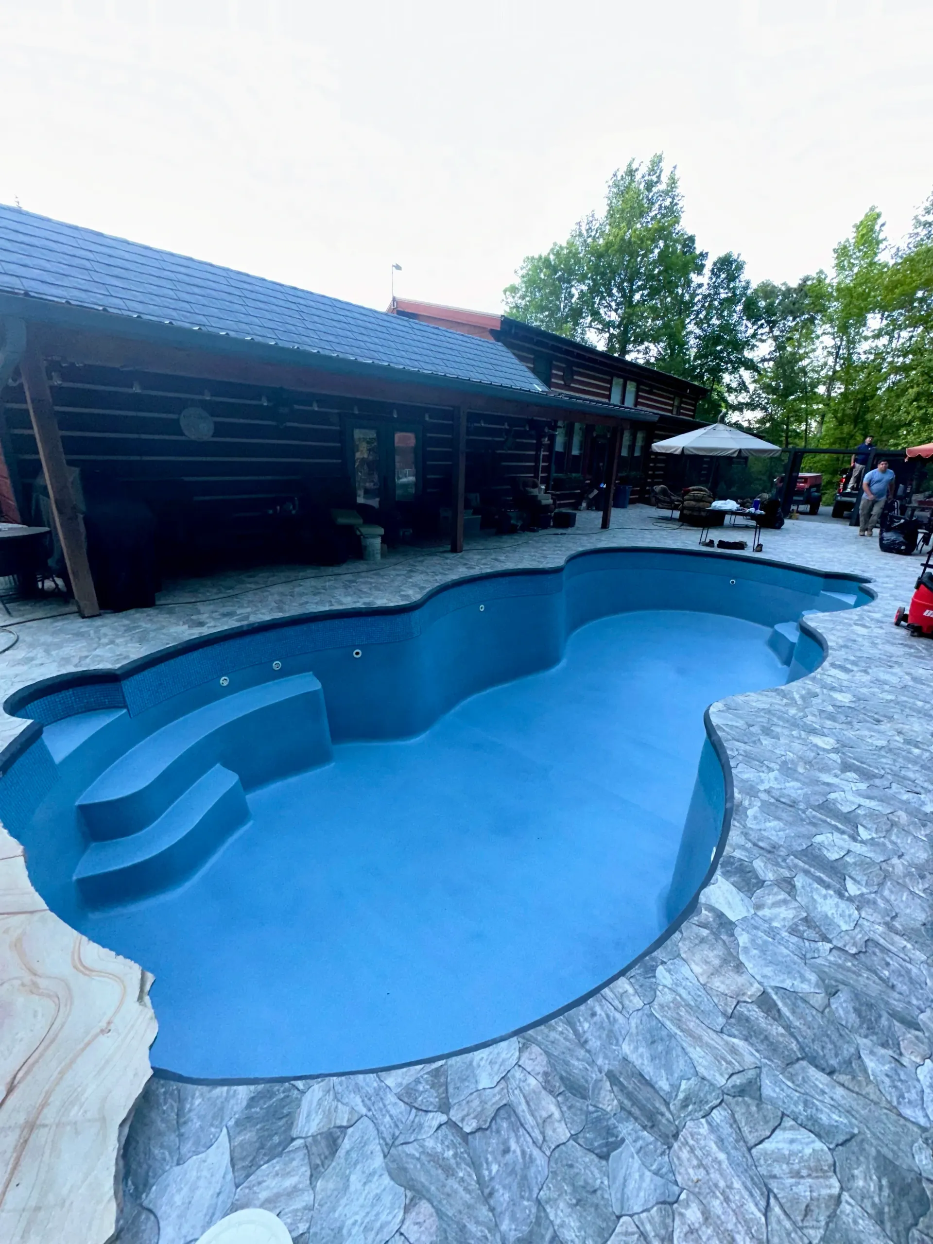 A large blue swimming pool is in the backyard of a house.