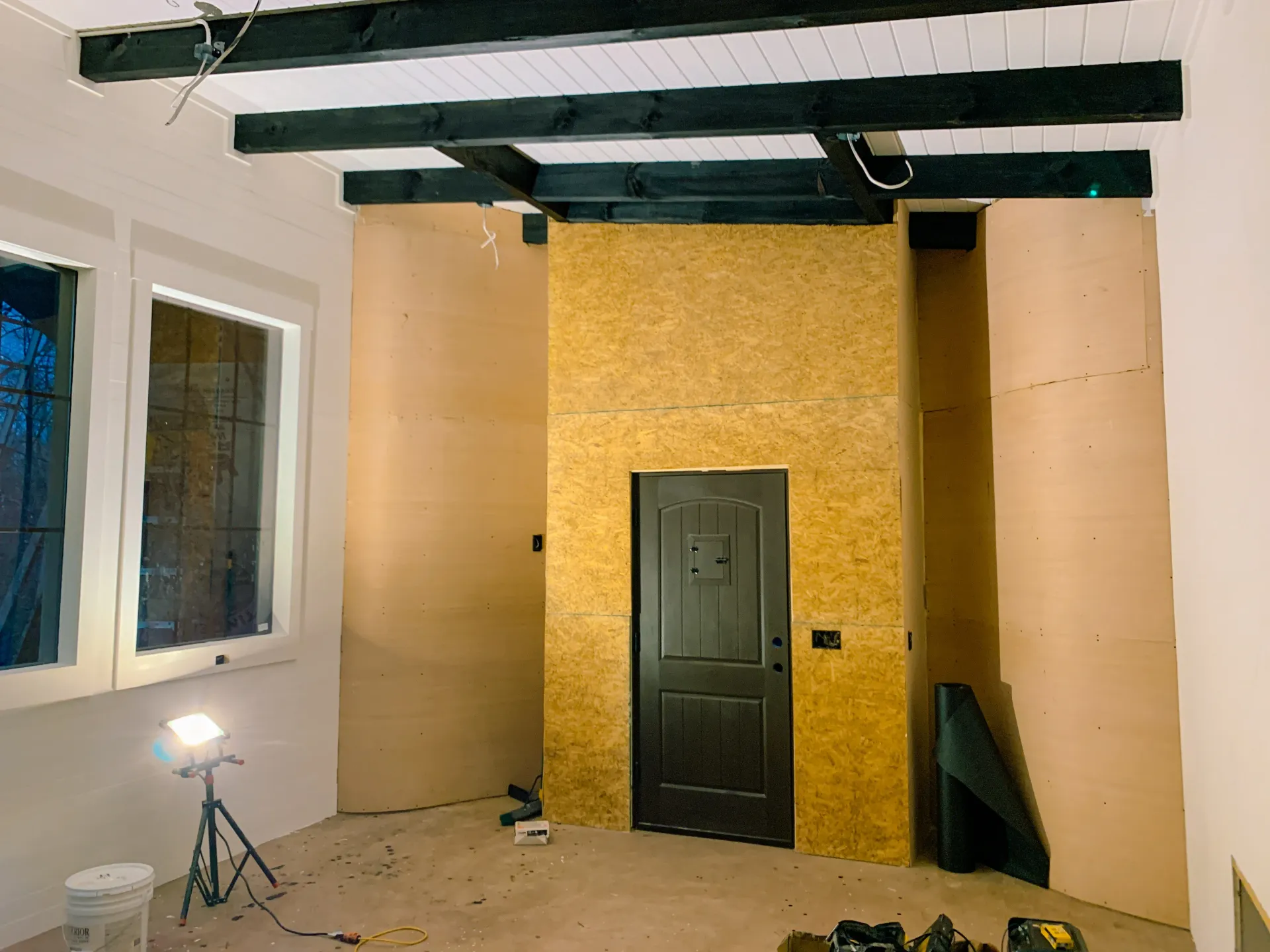 Unfinished she shed interior with black beams and plywood wall installation