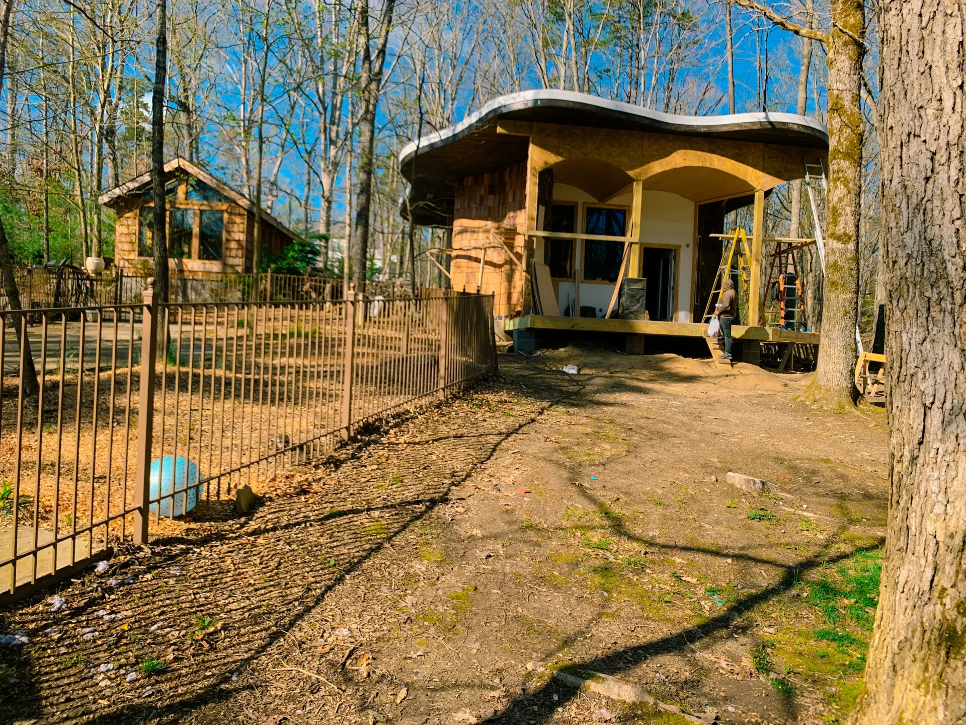 A small house in the middle of a forest with a fence around it. $