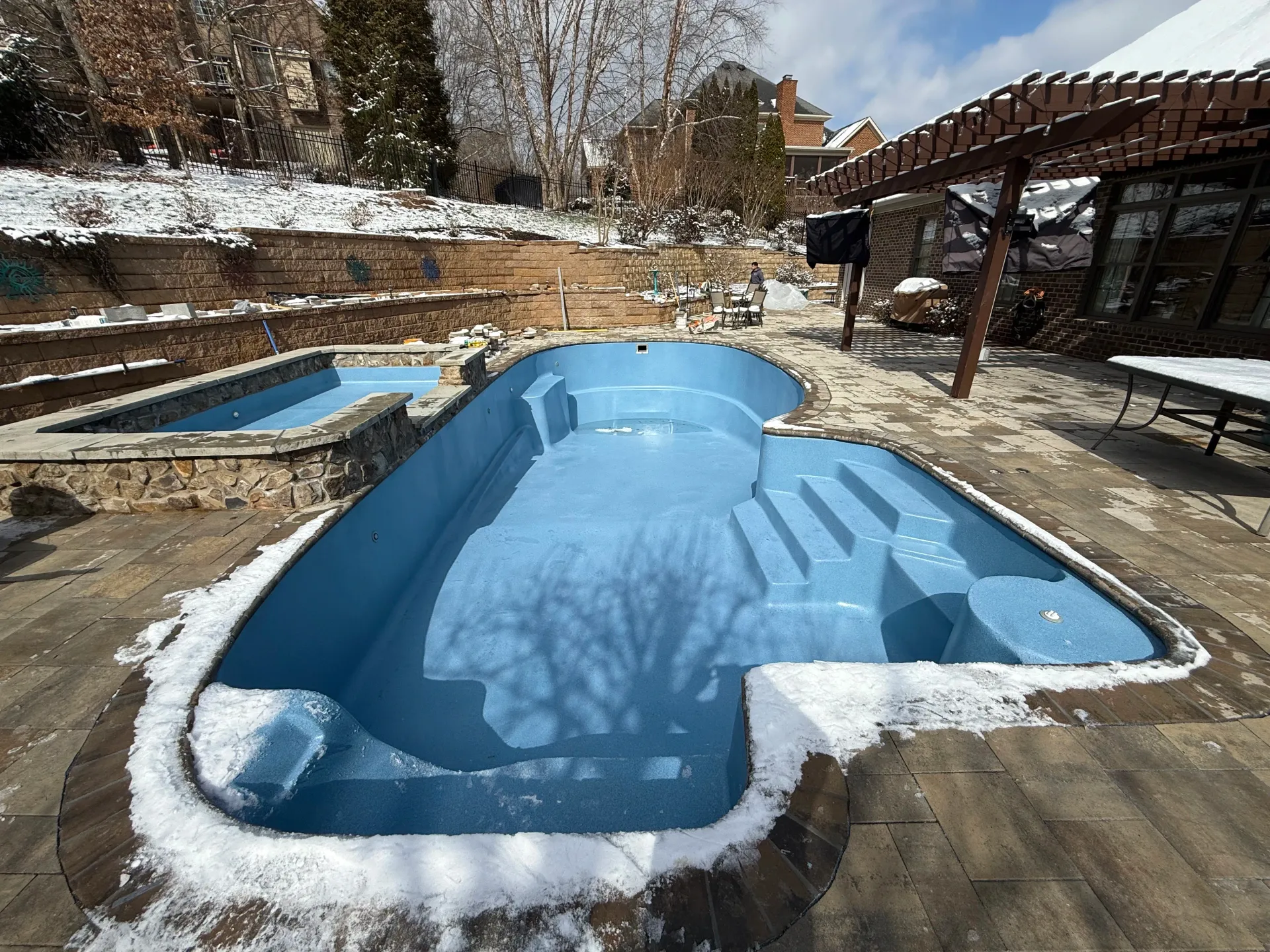 A large blue swimming pool is surrounded by snow