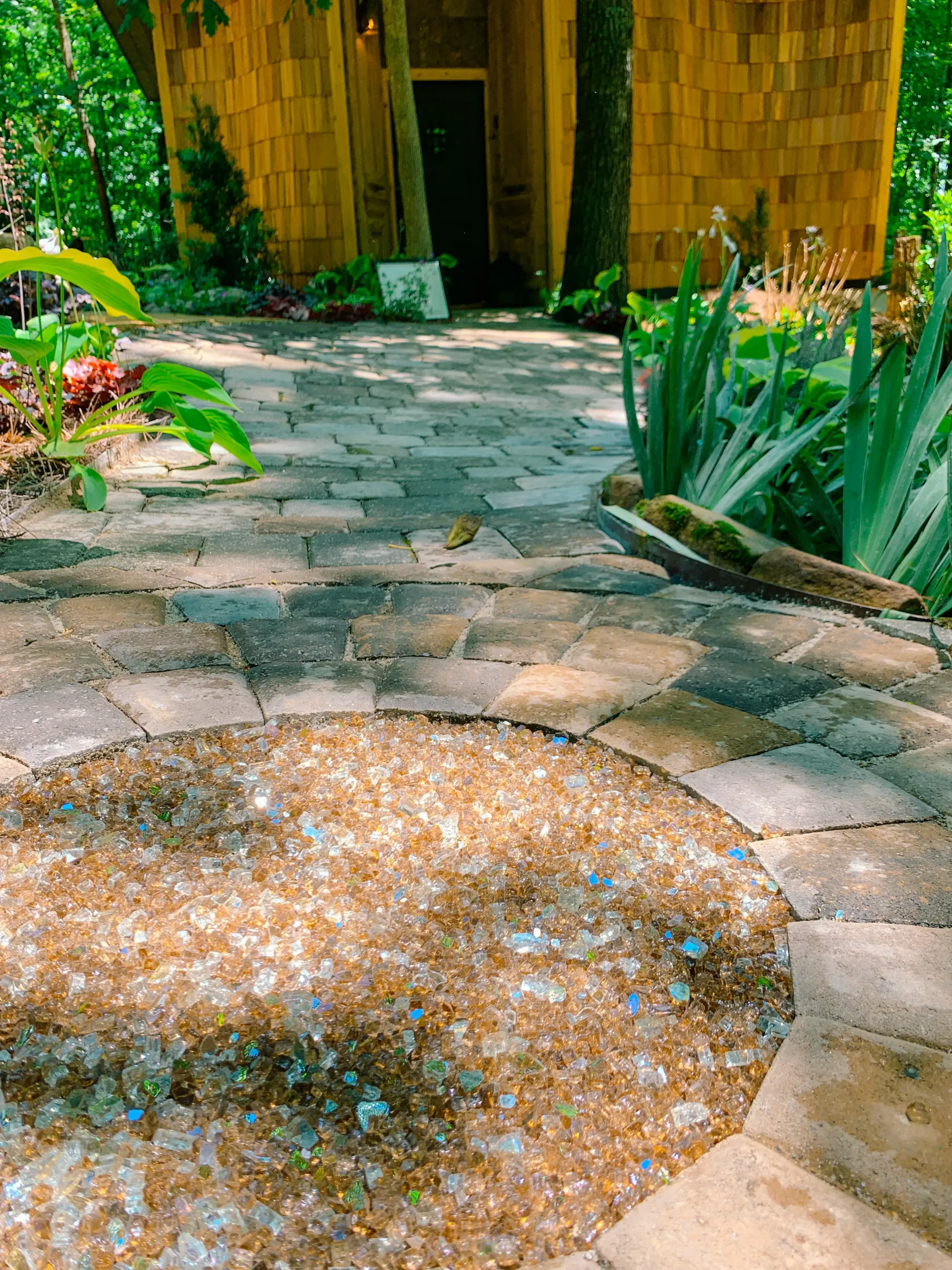 Bronze glass-filled circular fire pit along garden walkway