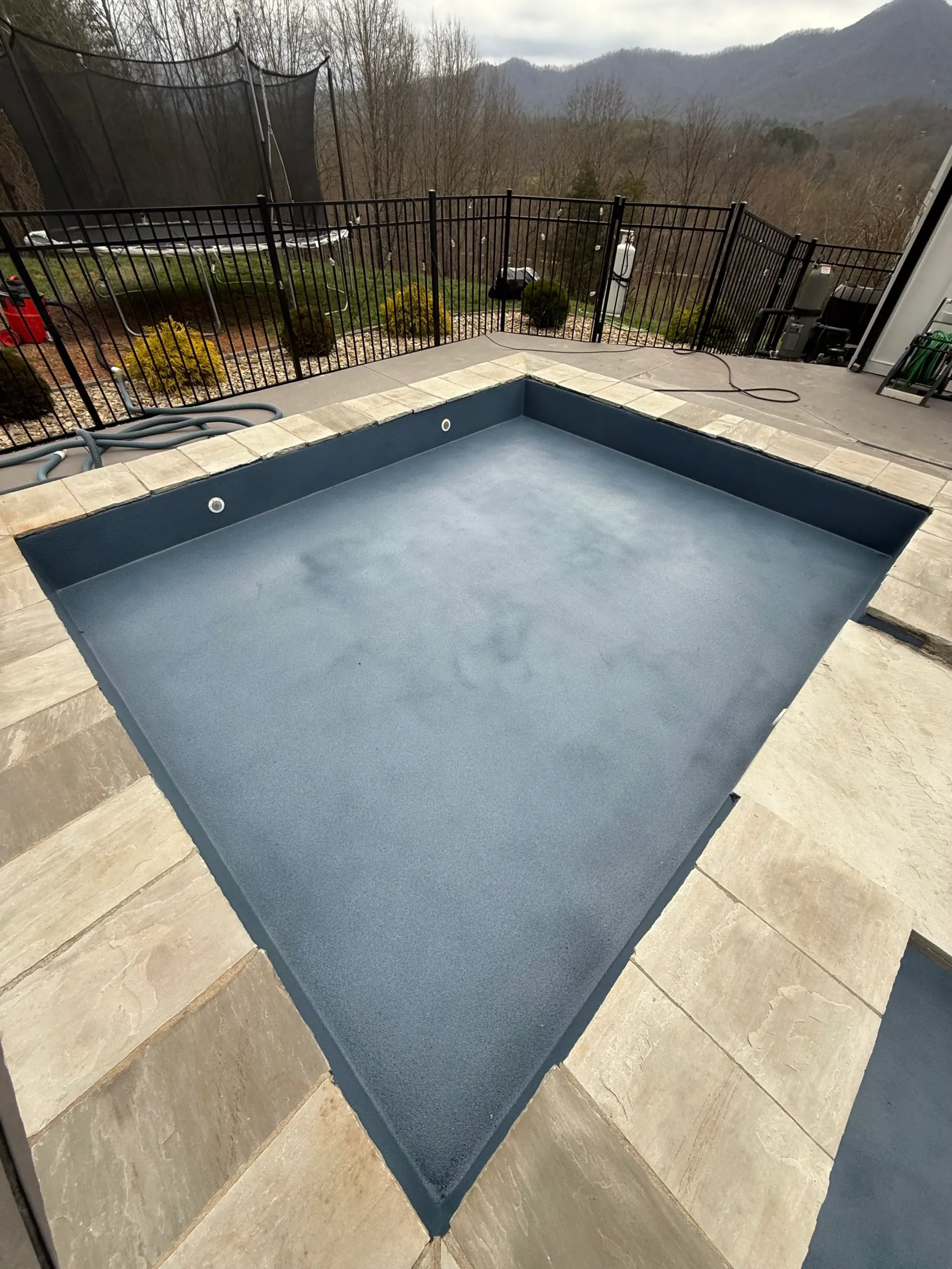 A large swimming pool with a fence and mountains in the background.