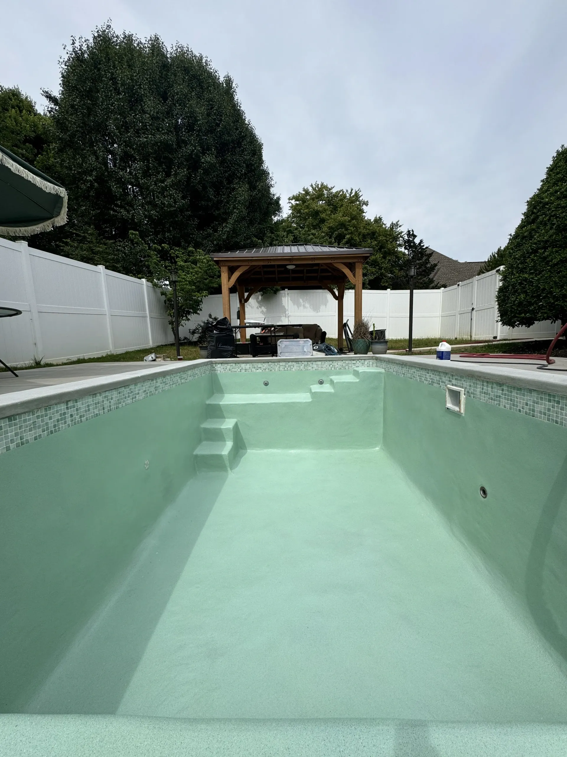 An empty swimming pool with a gazebo in the background.