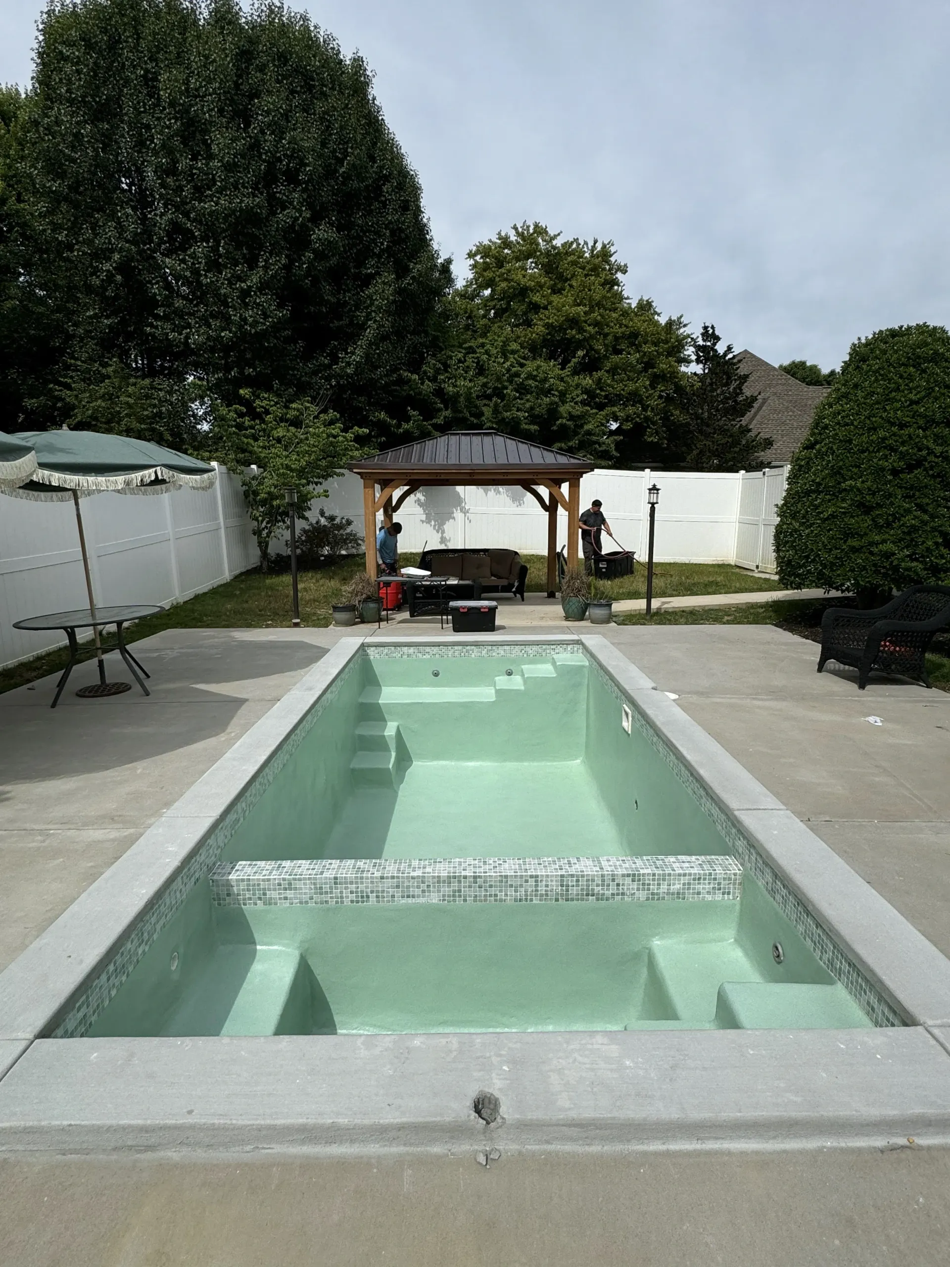 A large swimming pool in a backyard with a gazebo in the background.