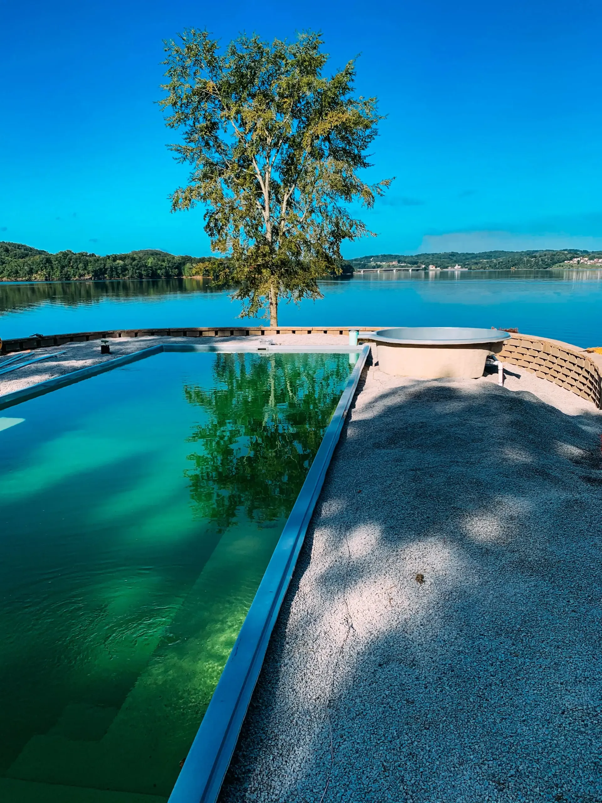 A swimming pool with a tree in the middle of it and a lake in the background.