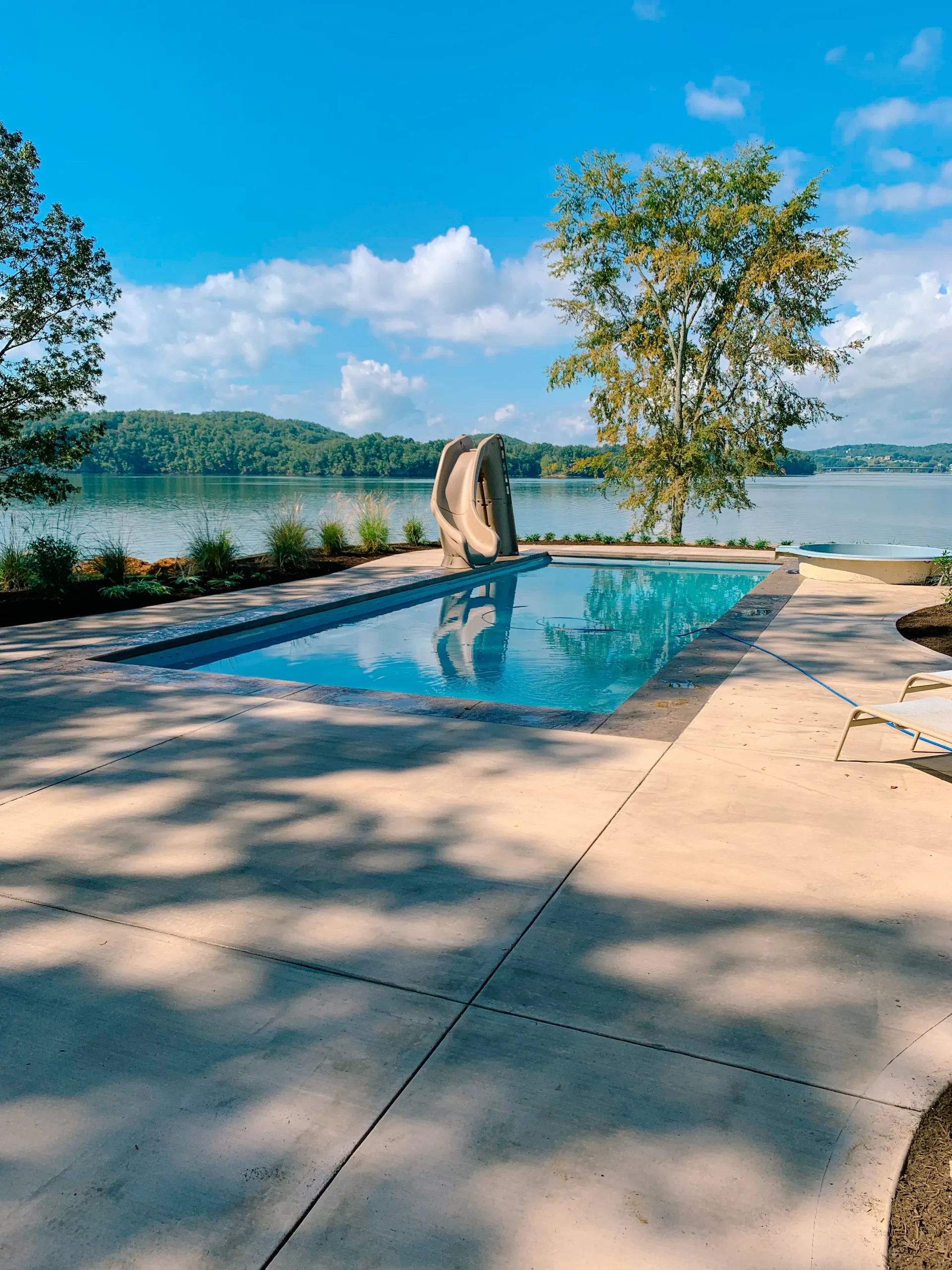 A large swimming pool is surrounded by trees and a lake.