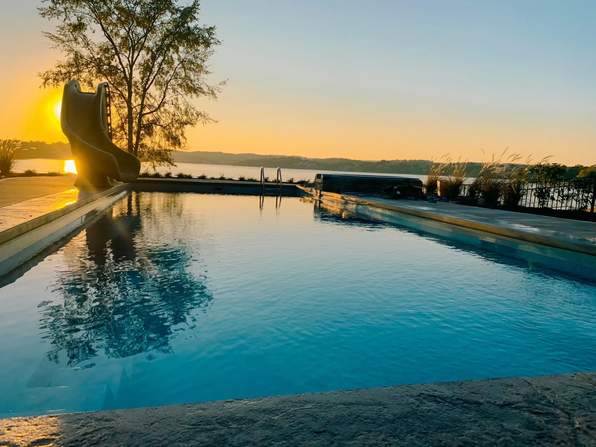 A large swimming pool with a slide in the background at sunset