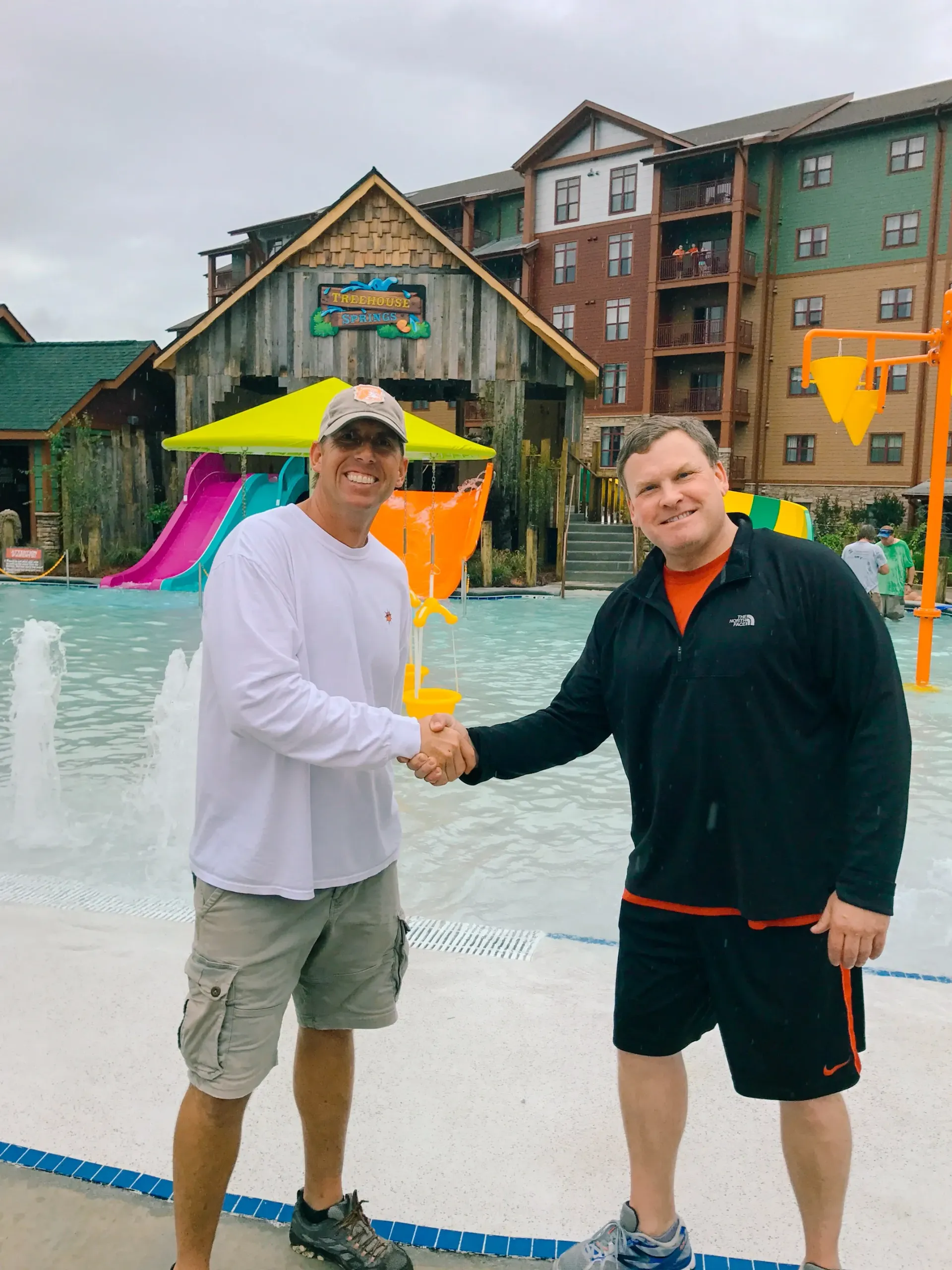 Two men shaking hands in front of a water park