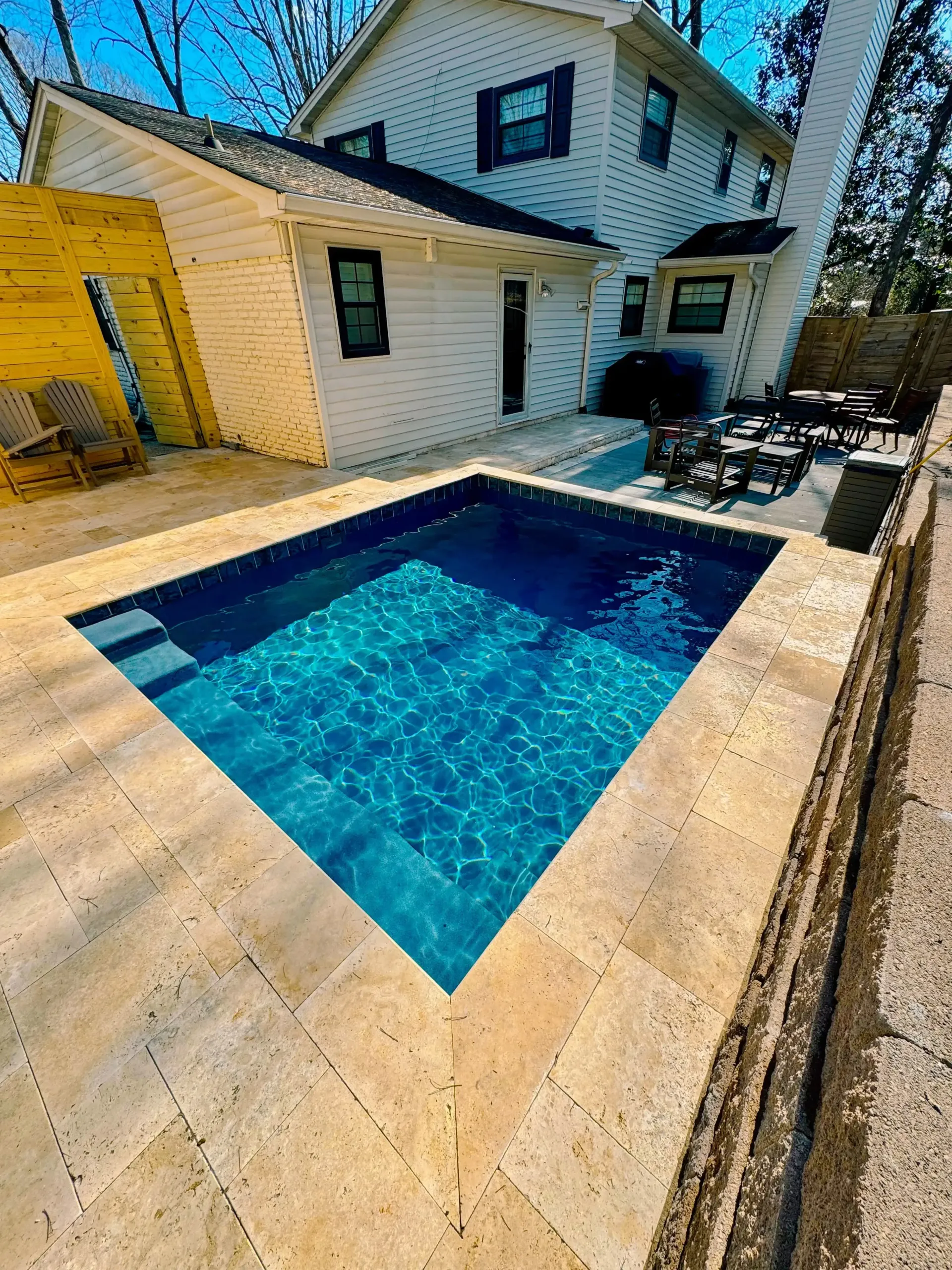 A small swimming pool is in the backyard of a house.