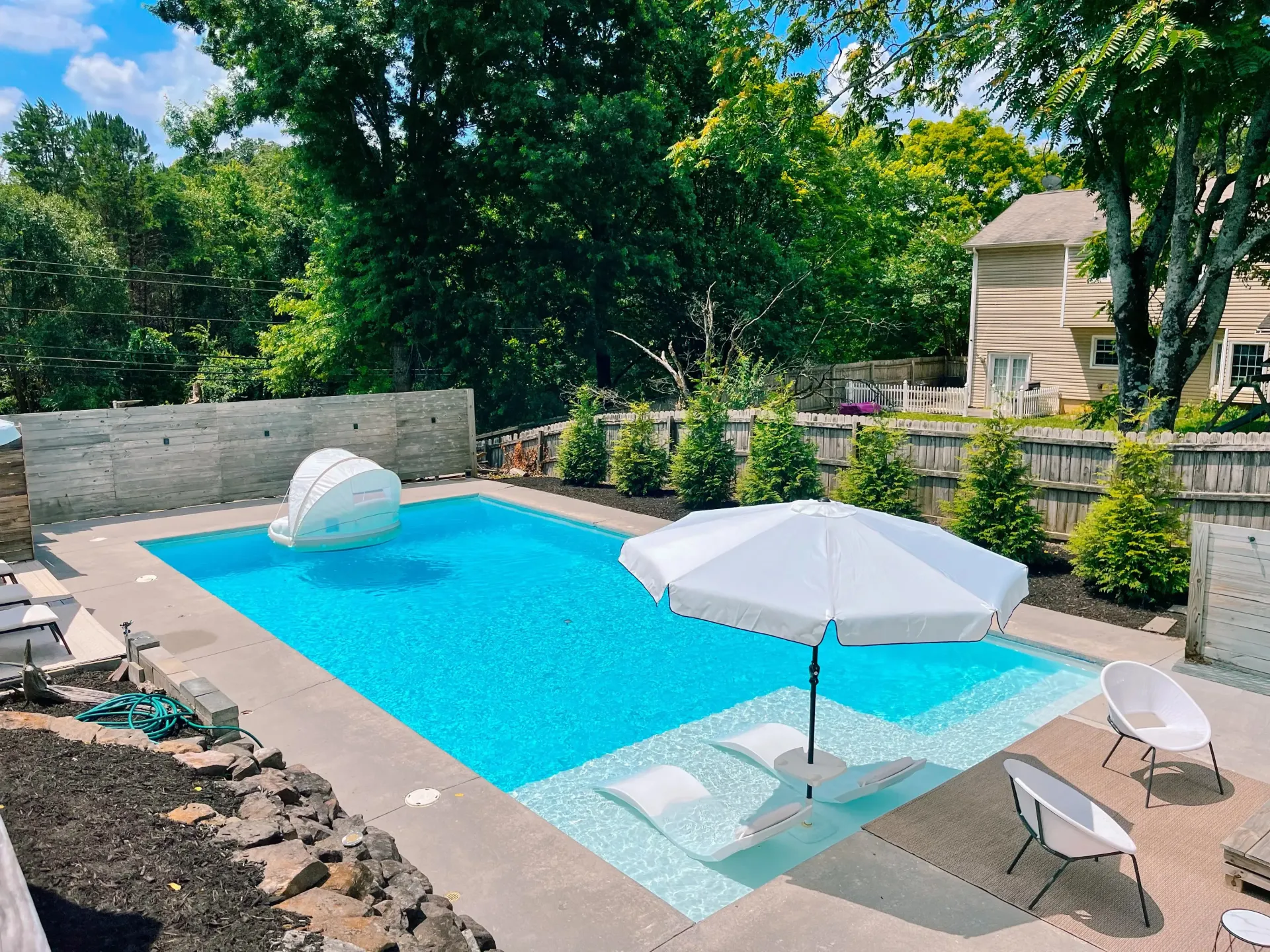 A large swimming pool with umbrellas and chairs in a backyard.