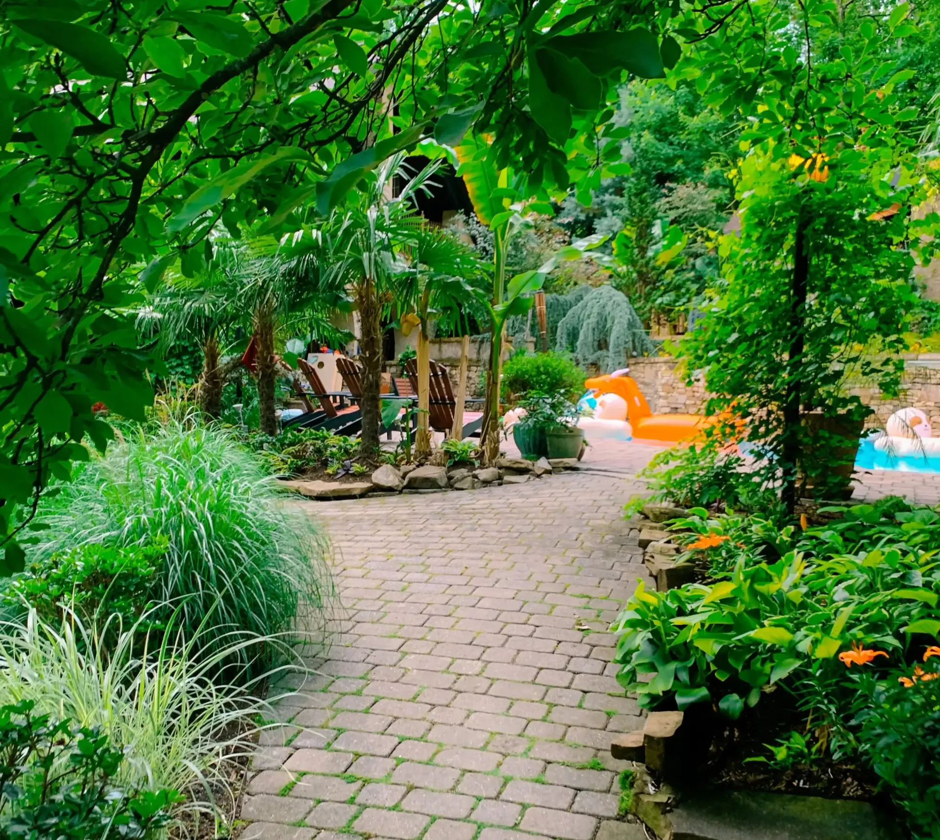 A brick walkway leading to a pool surrounded by trees