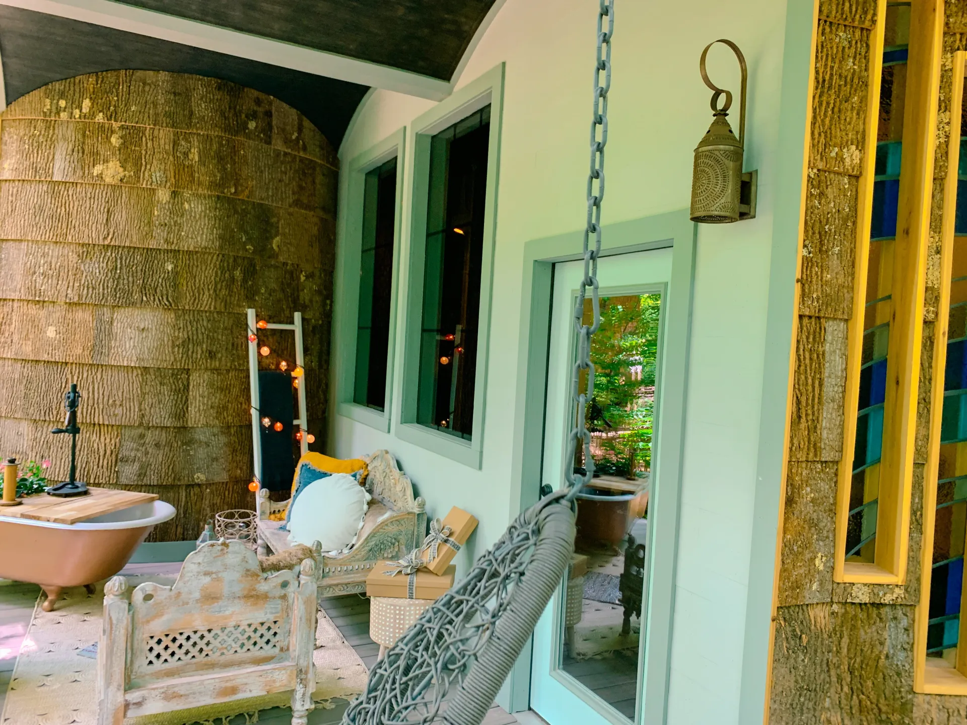 Rustic porch with carved wood bench and hanging chair beside bark wall siding