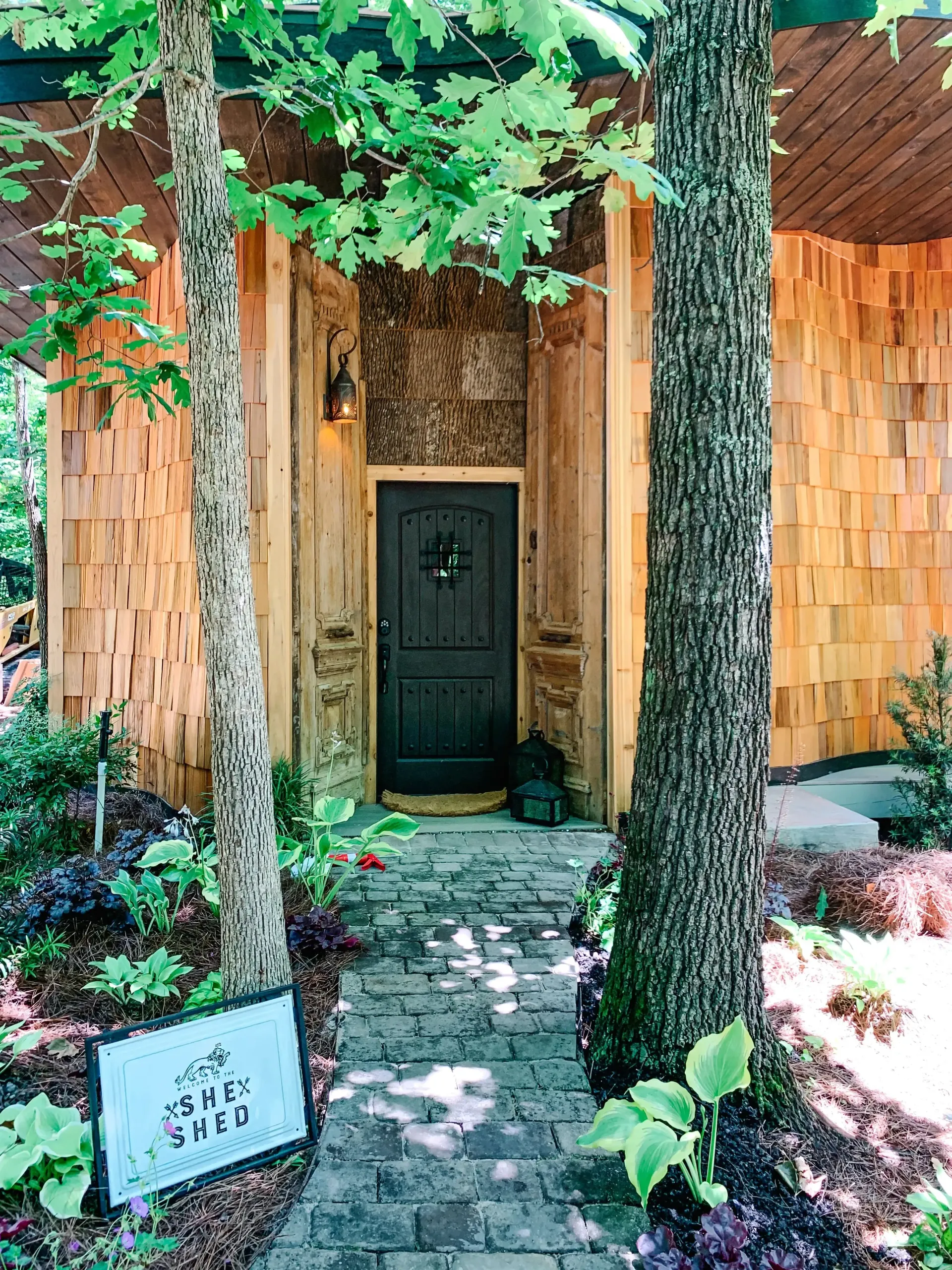 The front door of a house is surrounded by trees and a brick walkway.