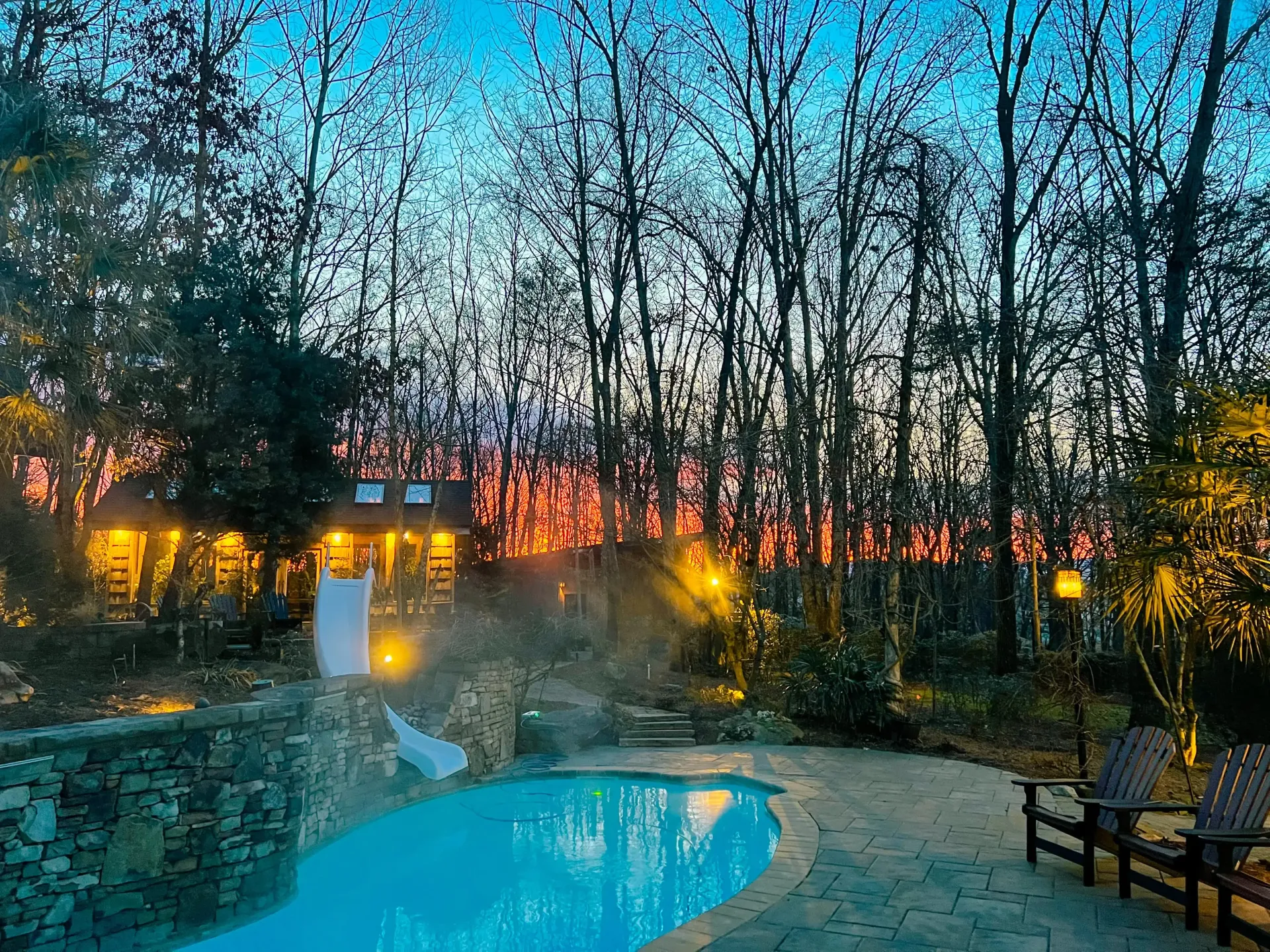 A large swimming pool is surrounded by trees at night.