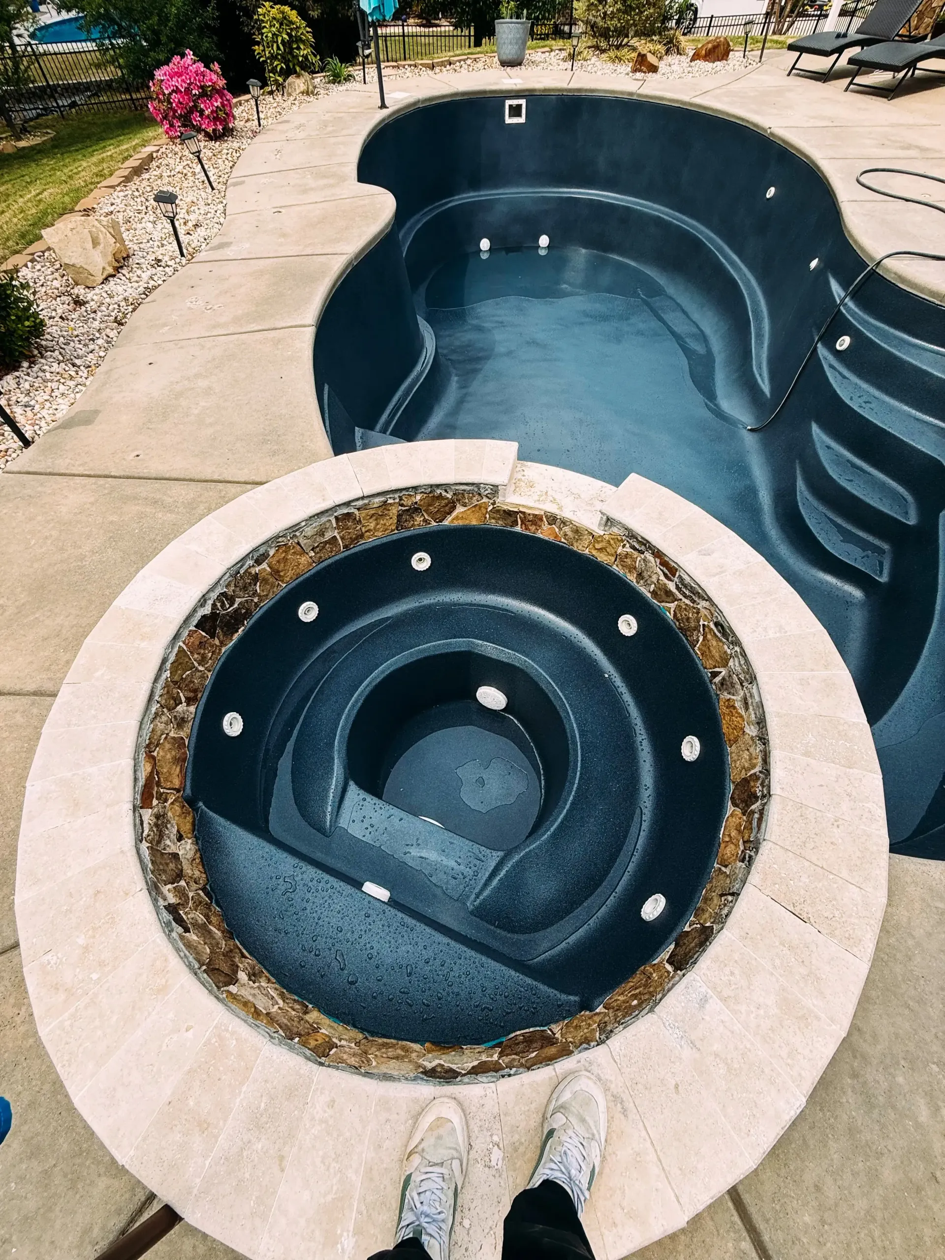 A person is standing next to a jacuzzi next to a swimming pool.